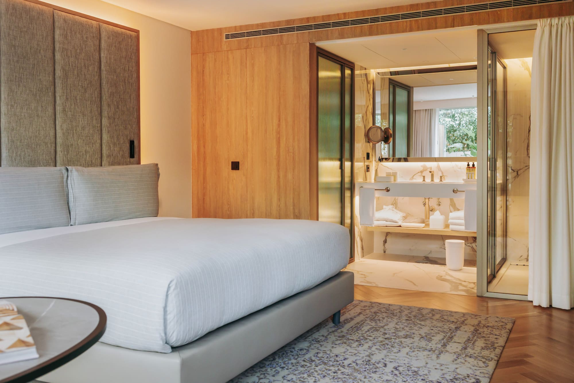 Modern hotel bedroom with king bed and open marble ensuite bathroom.