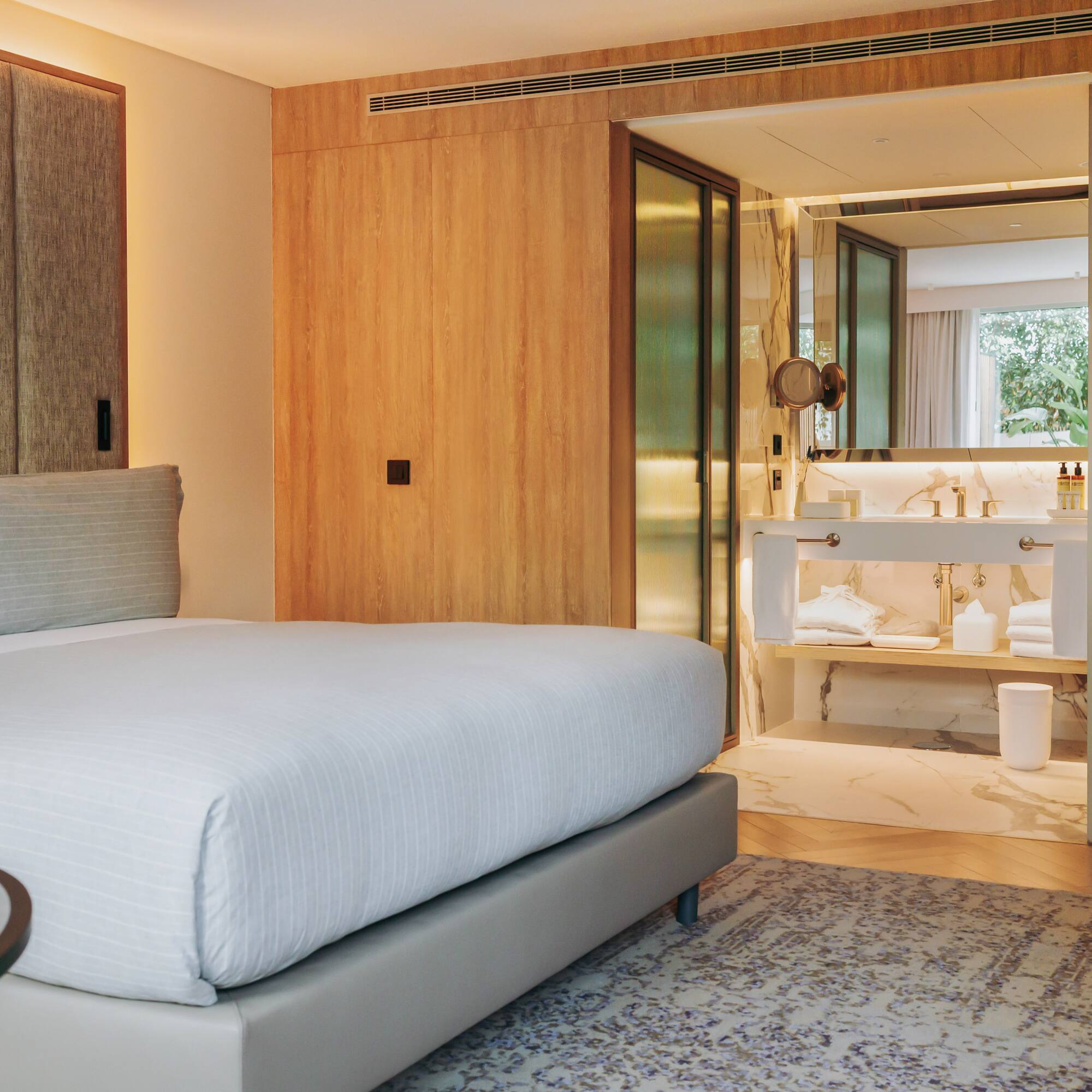Modern hotel bedroom with king bed and open marble ensuite bathroom.