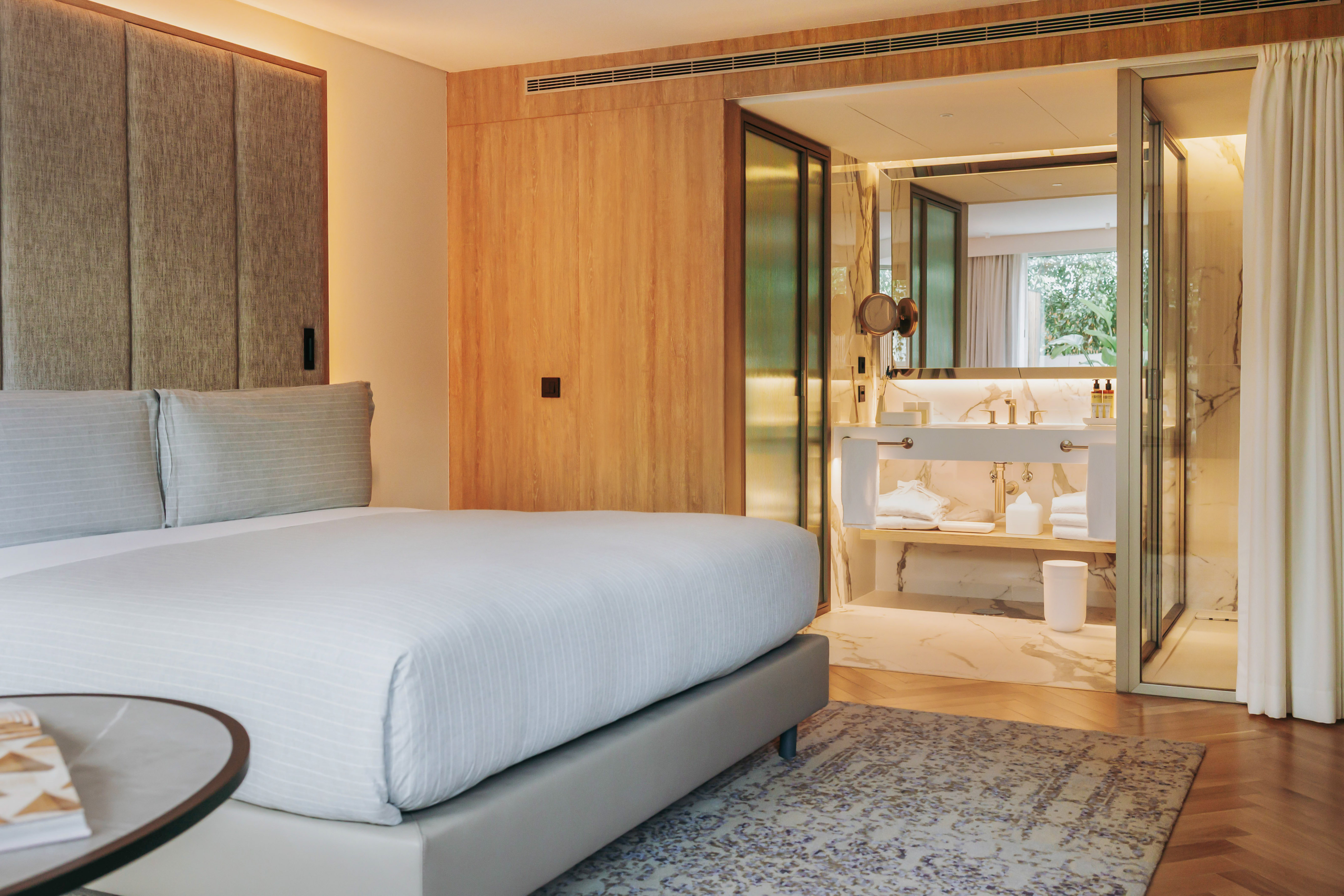 Modern luxury hotel room with king bed, wood paneling, and open marble bathroom.