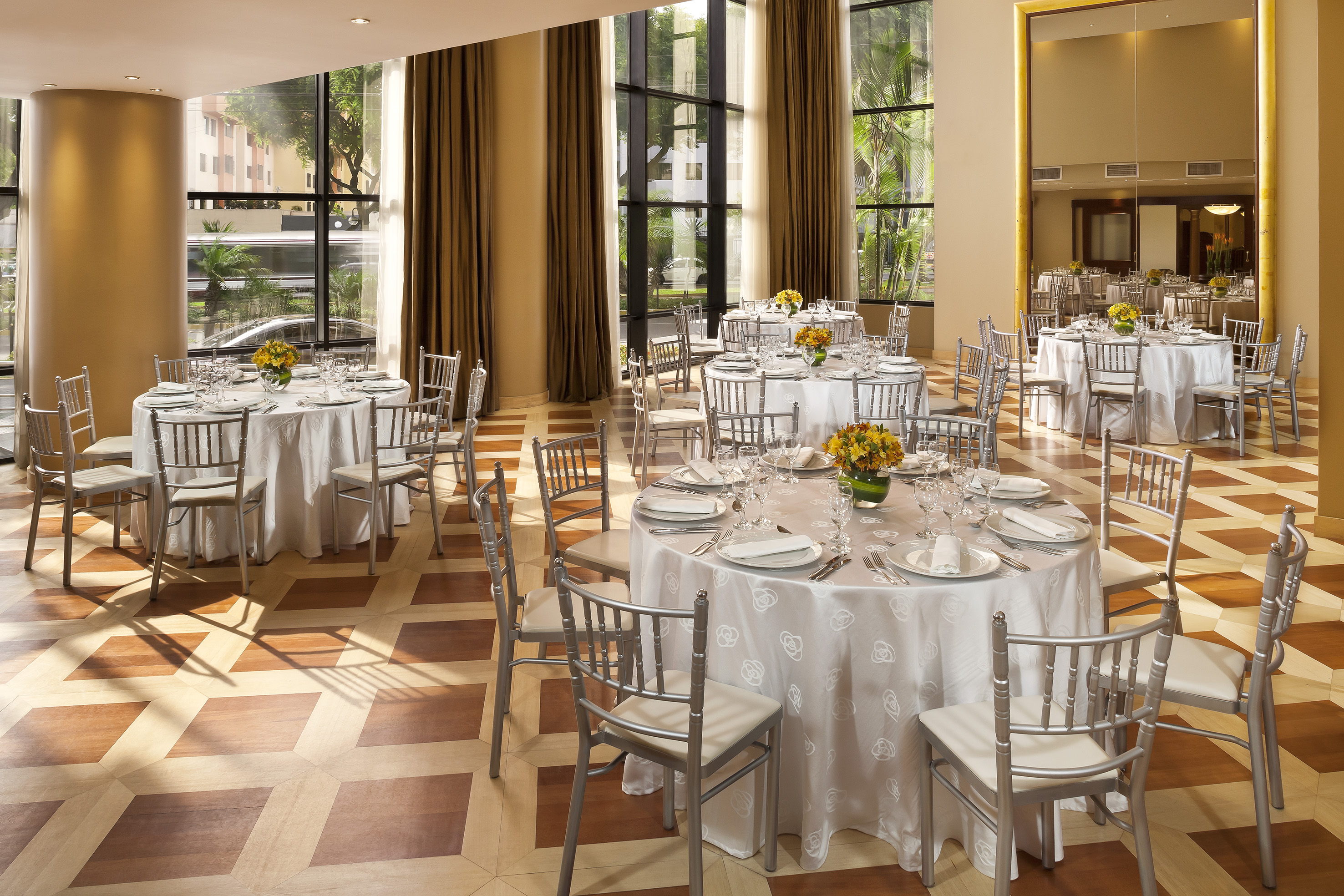 Elegant event space with round tables, silver chairs, and large windows.