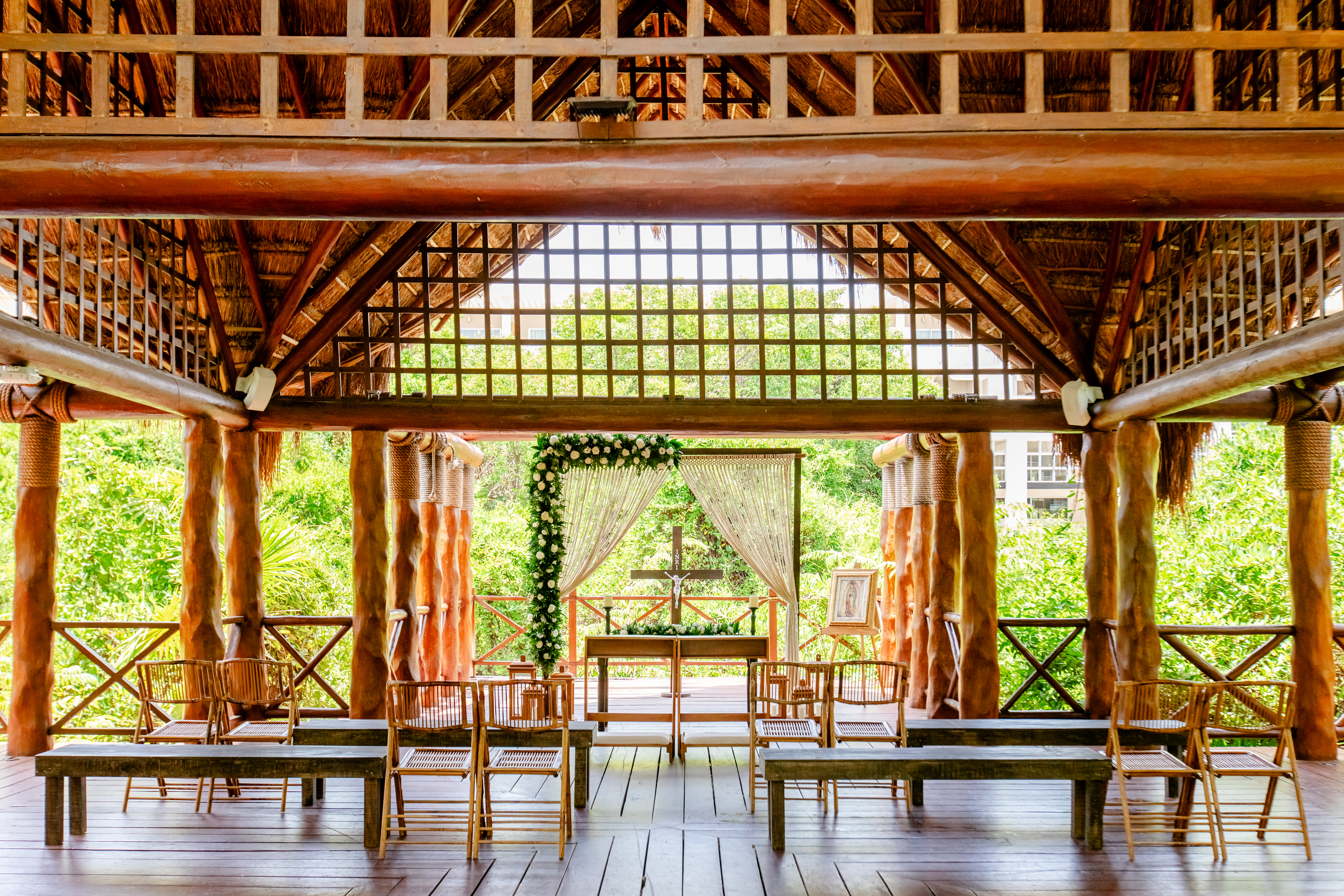 Wooden tropical outdoor wedding chapel with altar, cross, and floral decor.