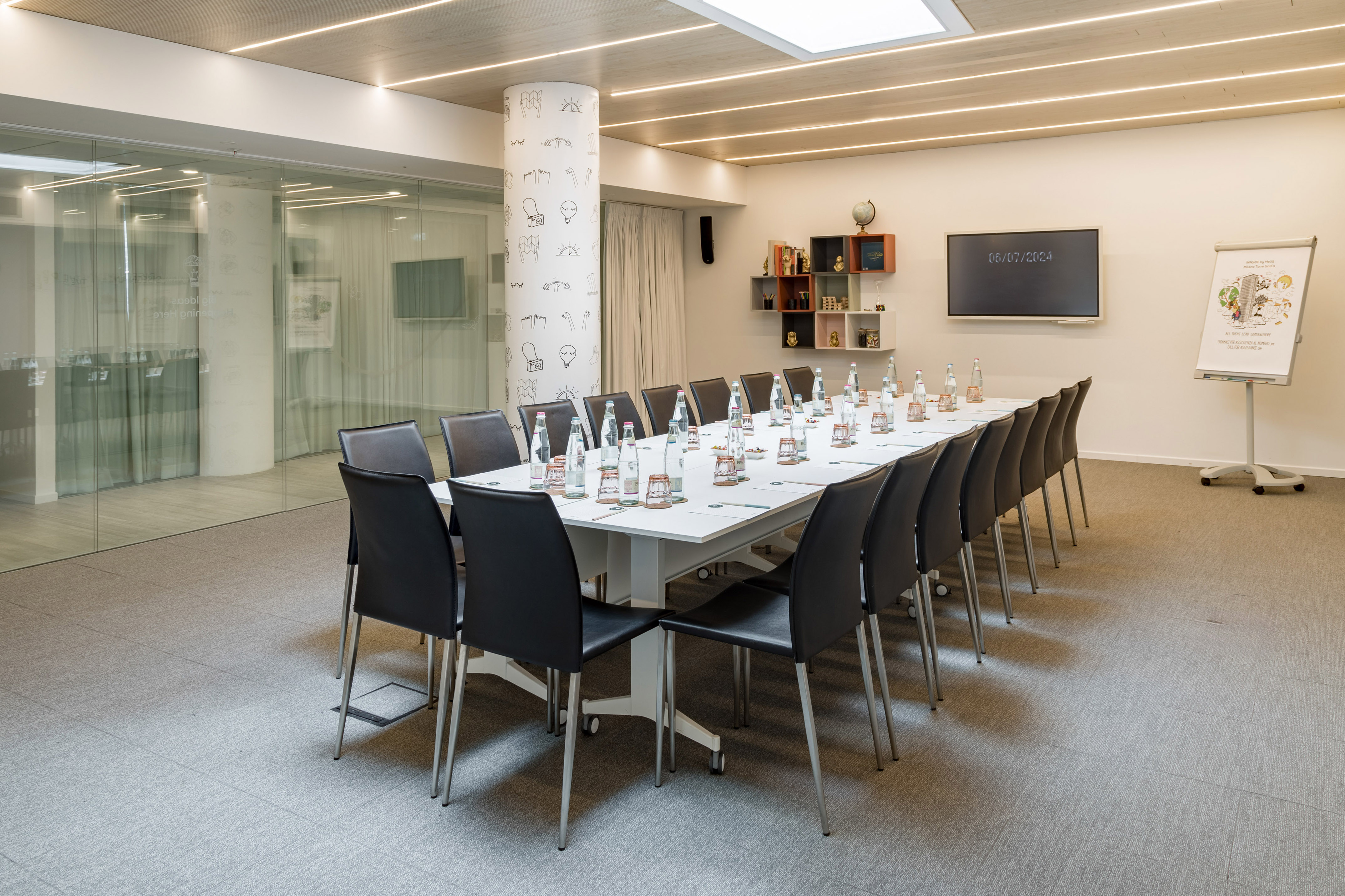 Modern meeting room with long table, black chairs, screen, and flip chart.