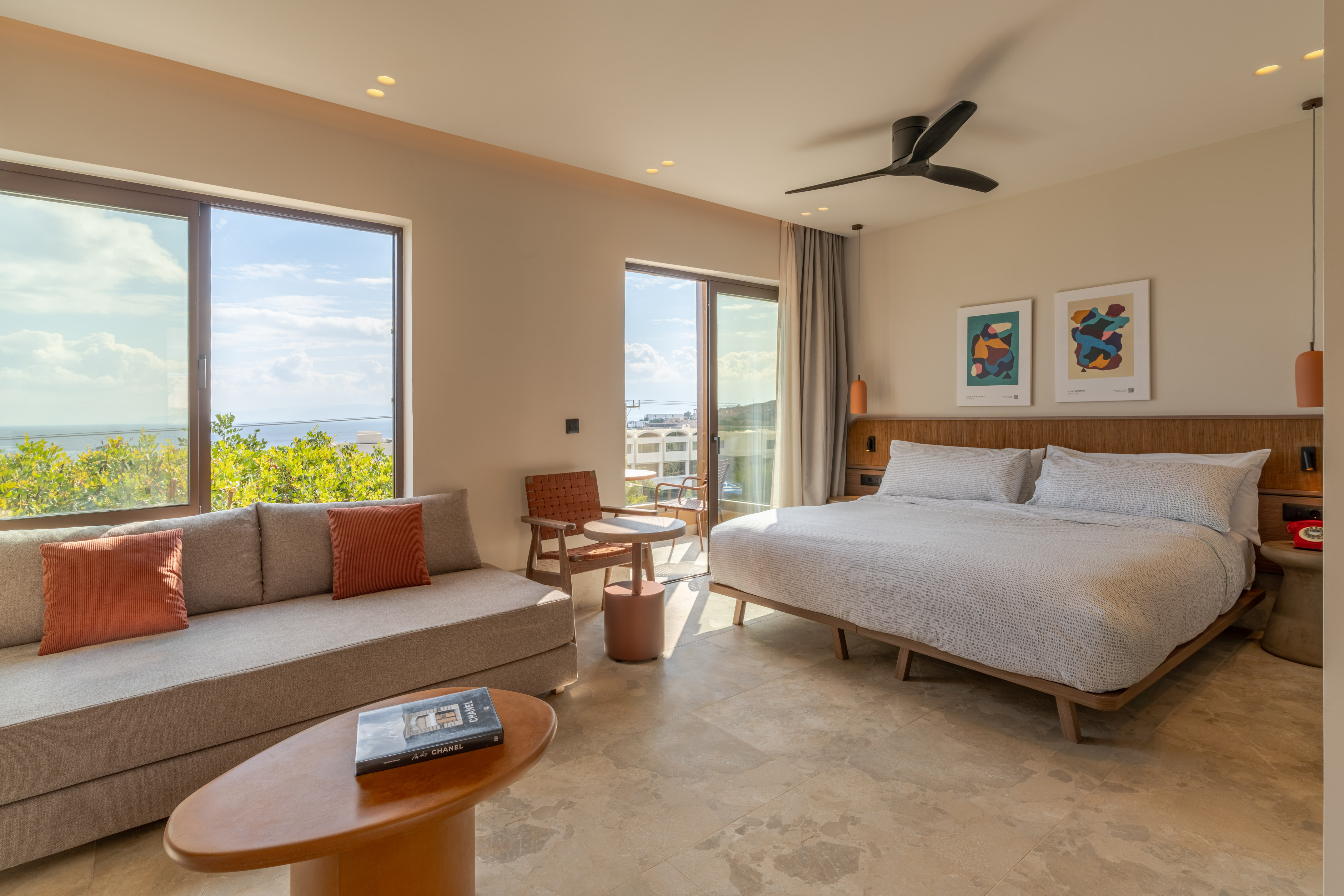 Modern hotel bedroom with ocean view, large bed, sofa, and balcony.