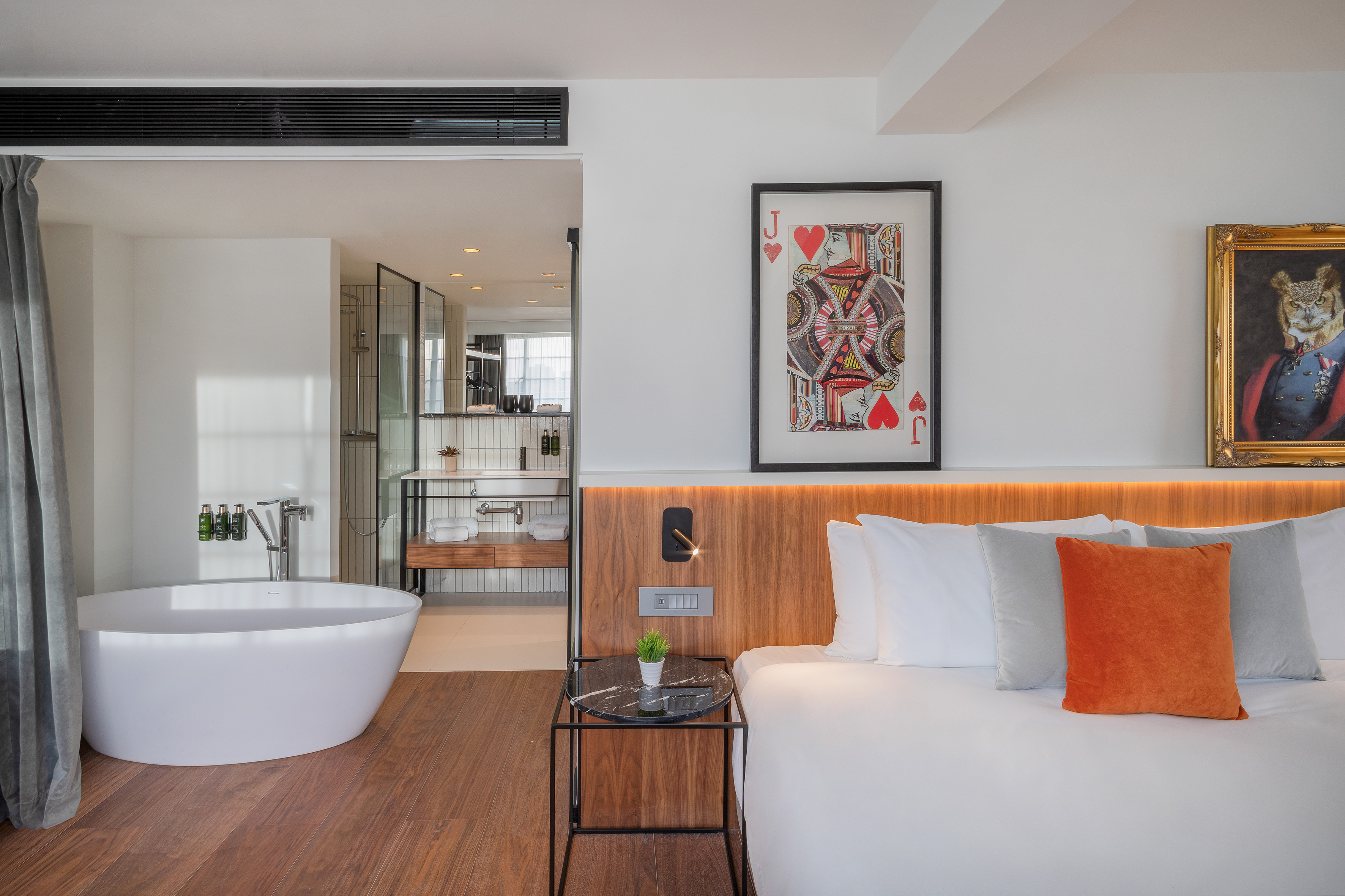 Modern hotel bedroom with open bathroom, freestanding tub, and contemporary decor.