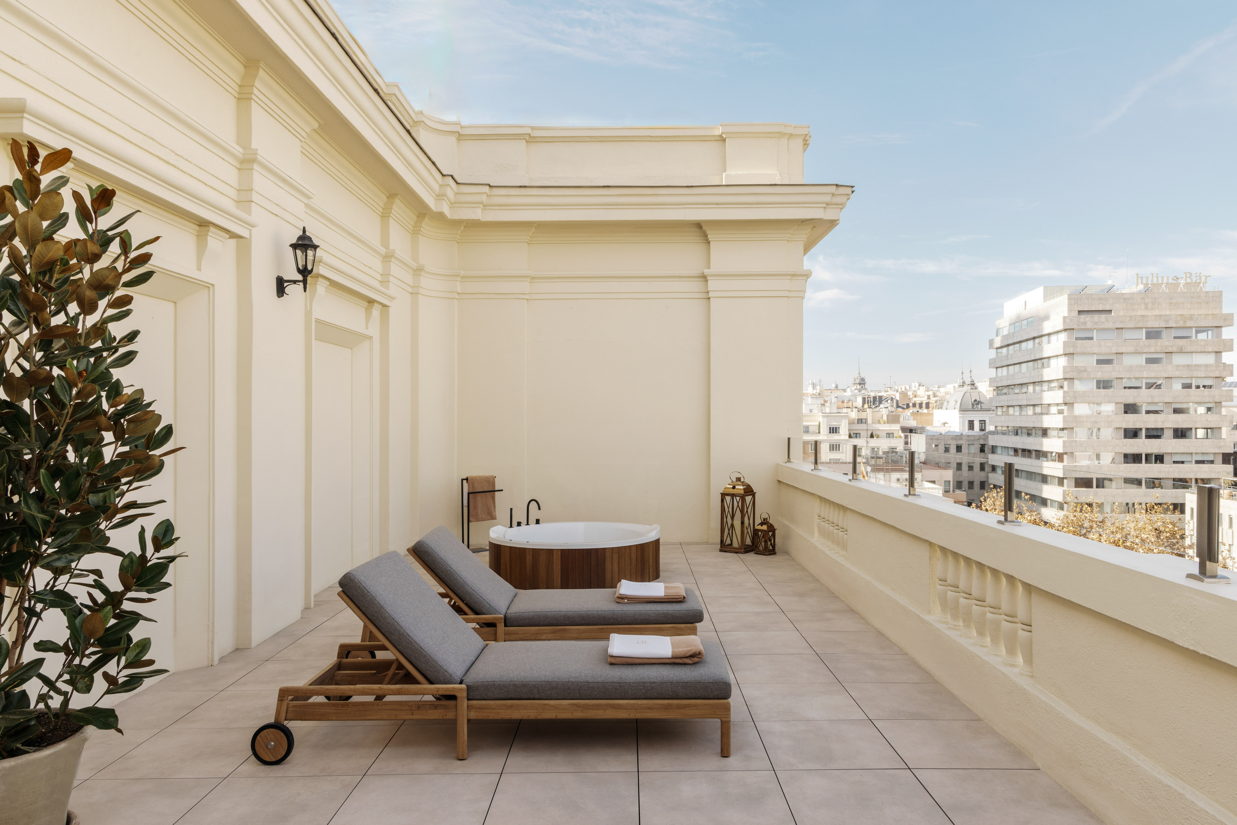 Luxury hotel rooftop terrace with jacuzzi, sun loungers, and urban skyline.