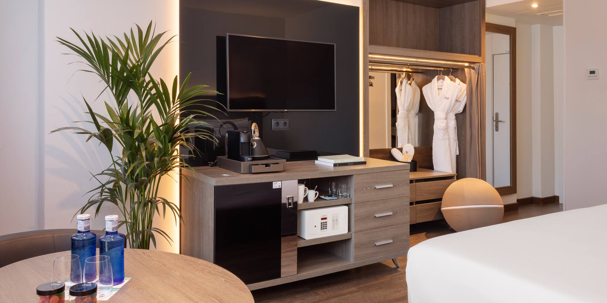 Modern hotel room with TV, coffee maker, minibar, safe, and bathrobes.