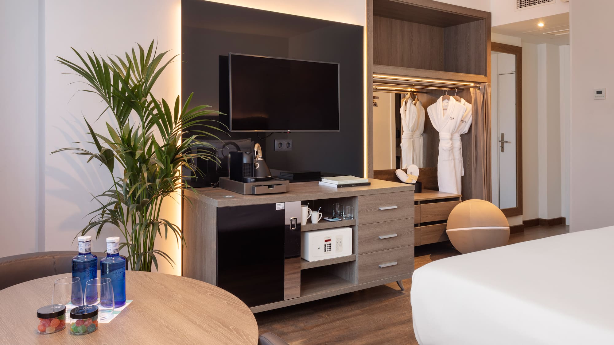 Modern hotel room with TV, coffee maker, minibar, safe, and bathrobes.