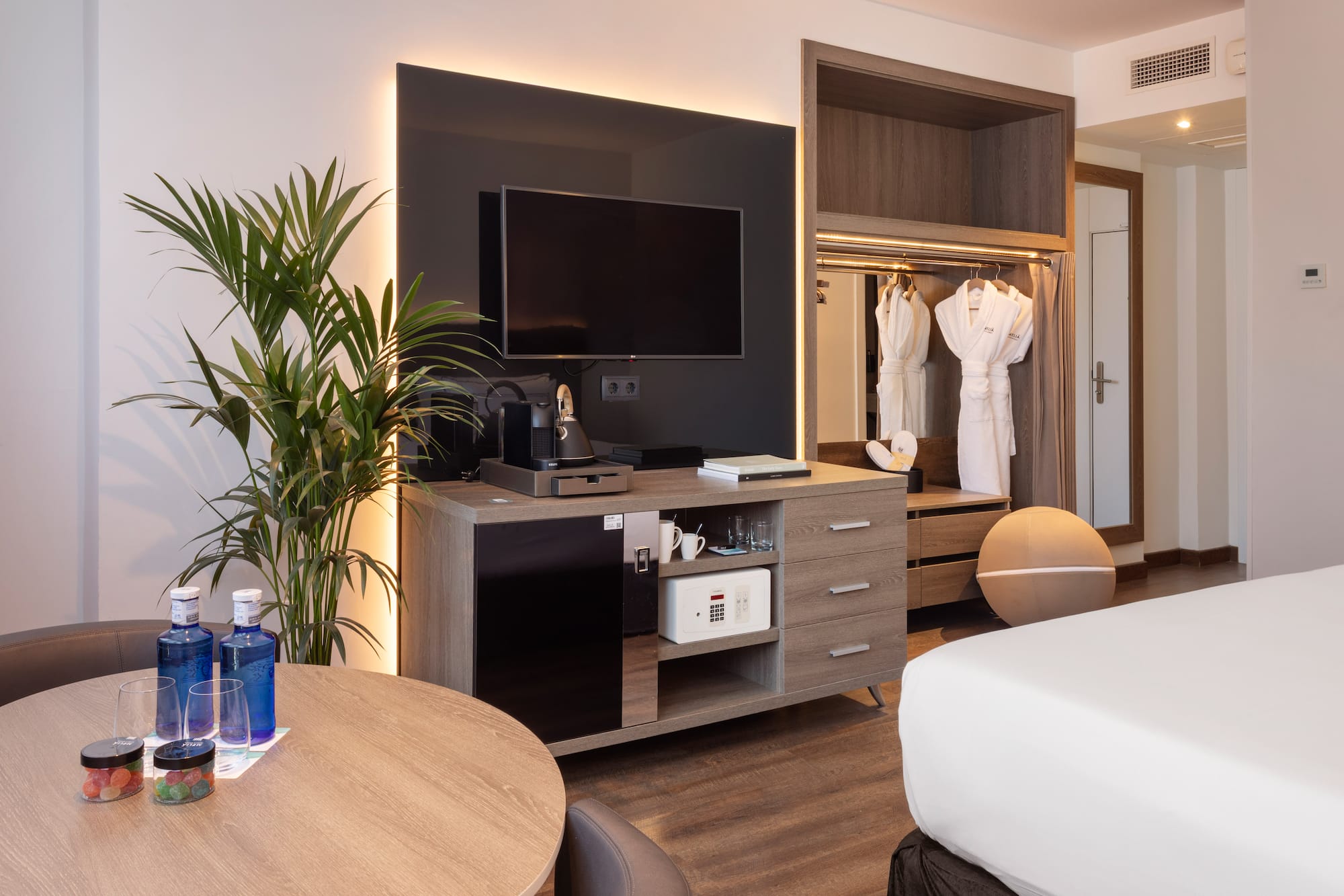 Modern hotel room with TV, coffee maker, minibar, safe, and bathrobes.