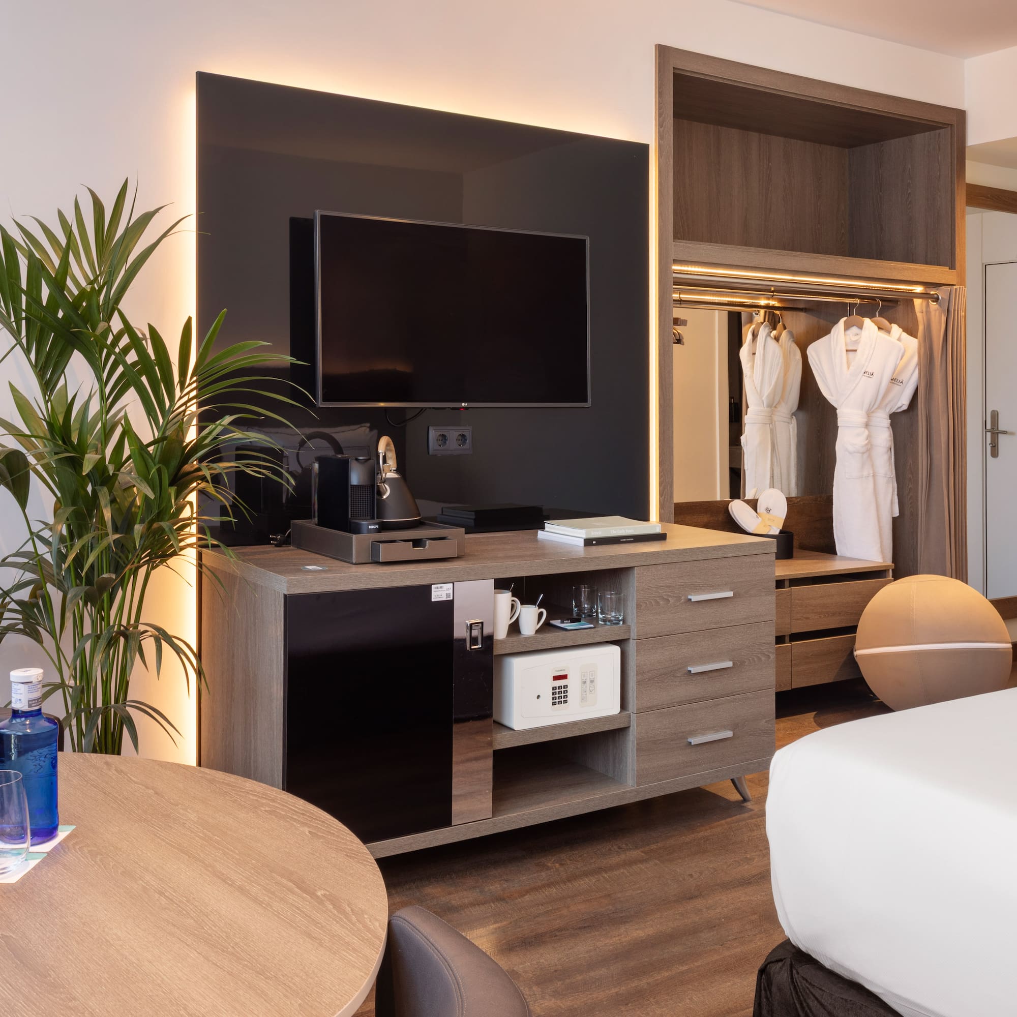 Contemporary hotel room with TV, mini-bar, open closet, bathrobes, and bed.