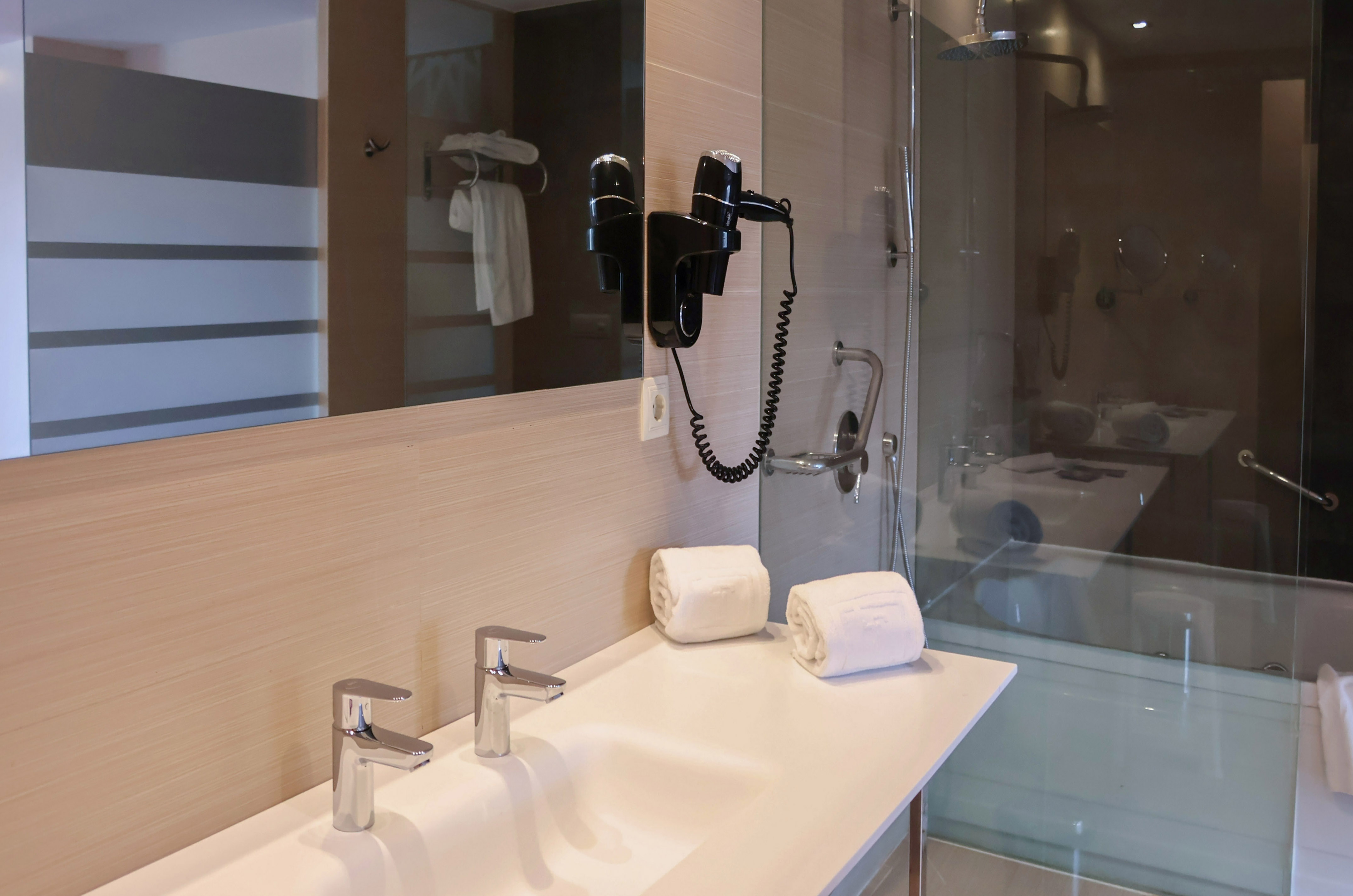 Modern hotel bathroom: double vanity, mirror, hairdryer, glass shower.