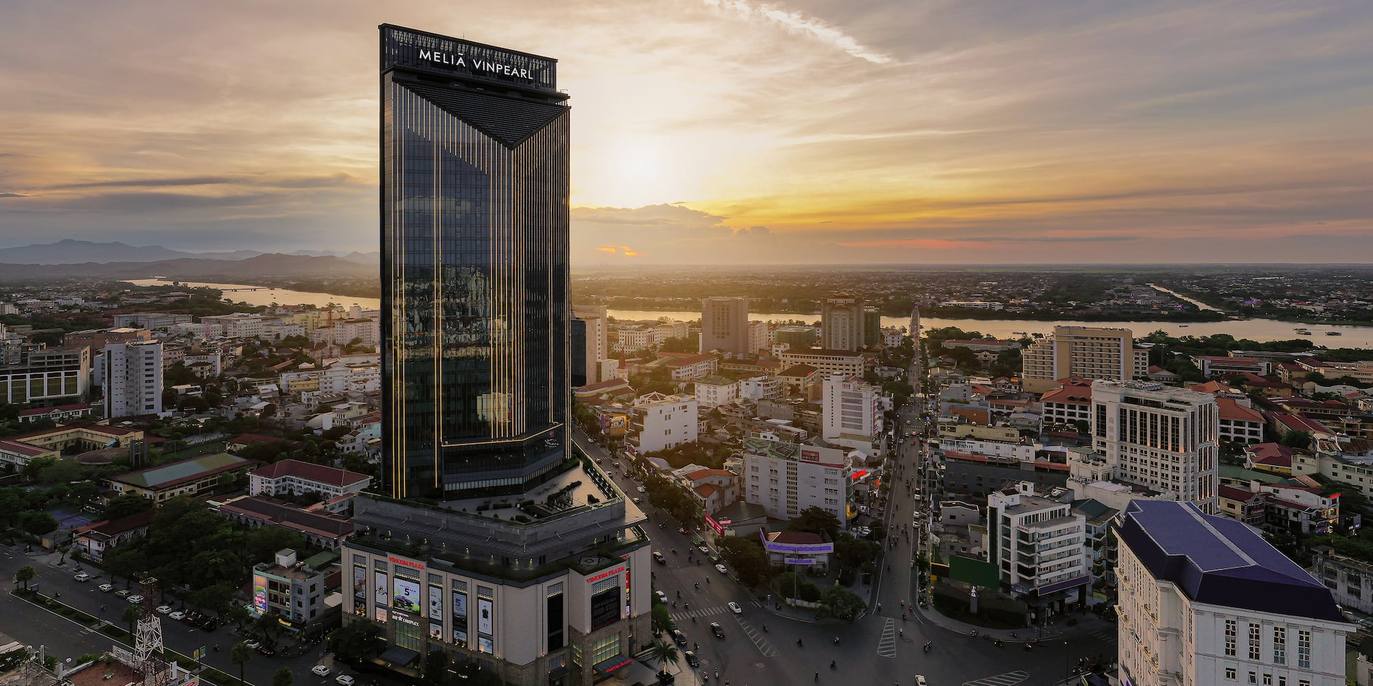 Melia Vinpearl hotel skyscraper at sunset overlooking a city and river.