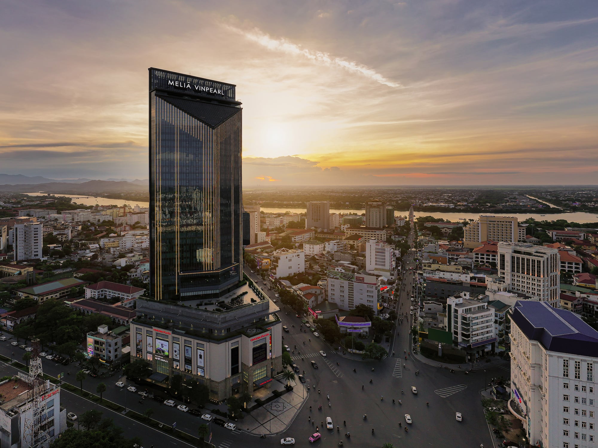 Melia Vinpearl hotel skyscraper at sunset overlooking a city and river.