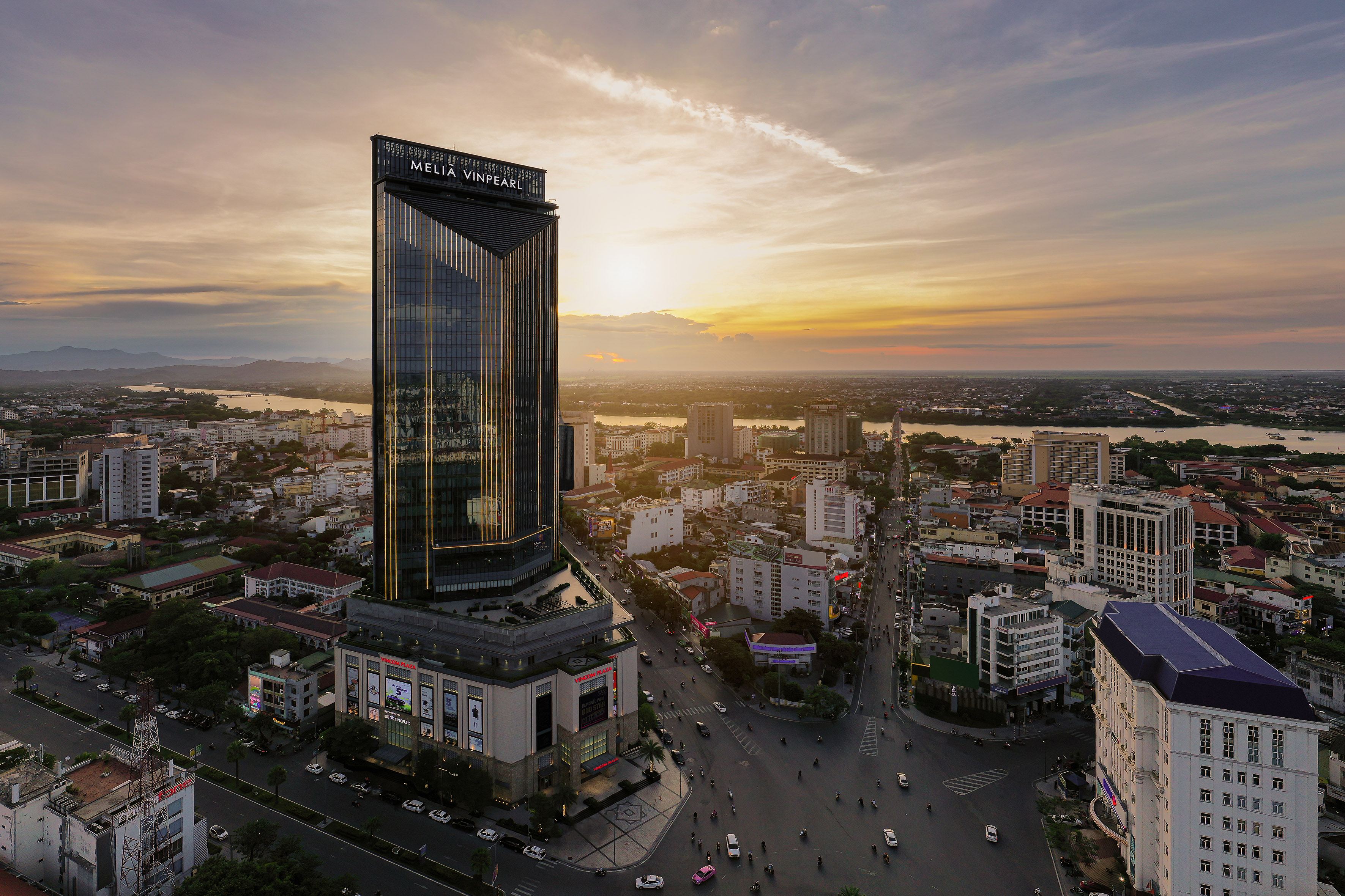 Melia Vinpearl hotel skyscraper at sunset overlooking a city and river.