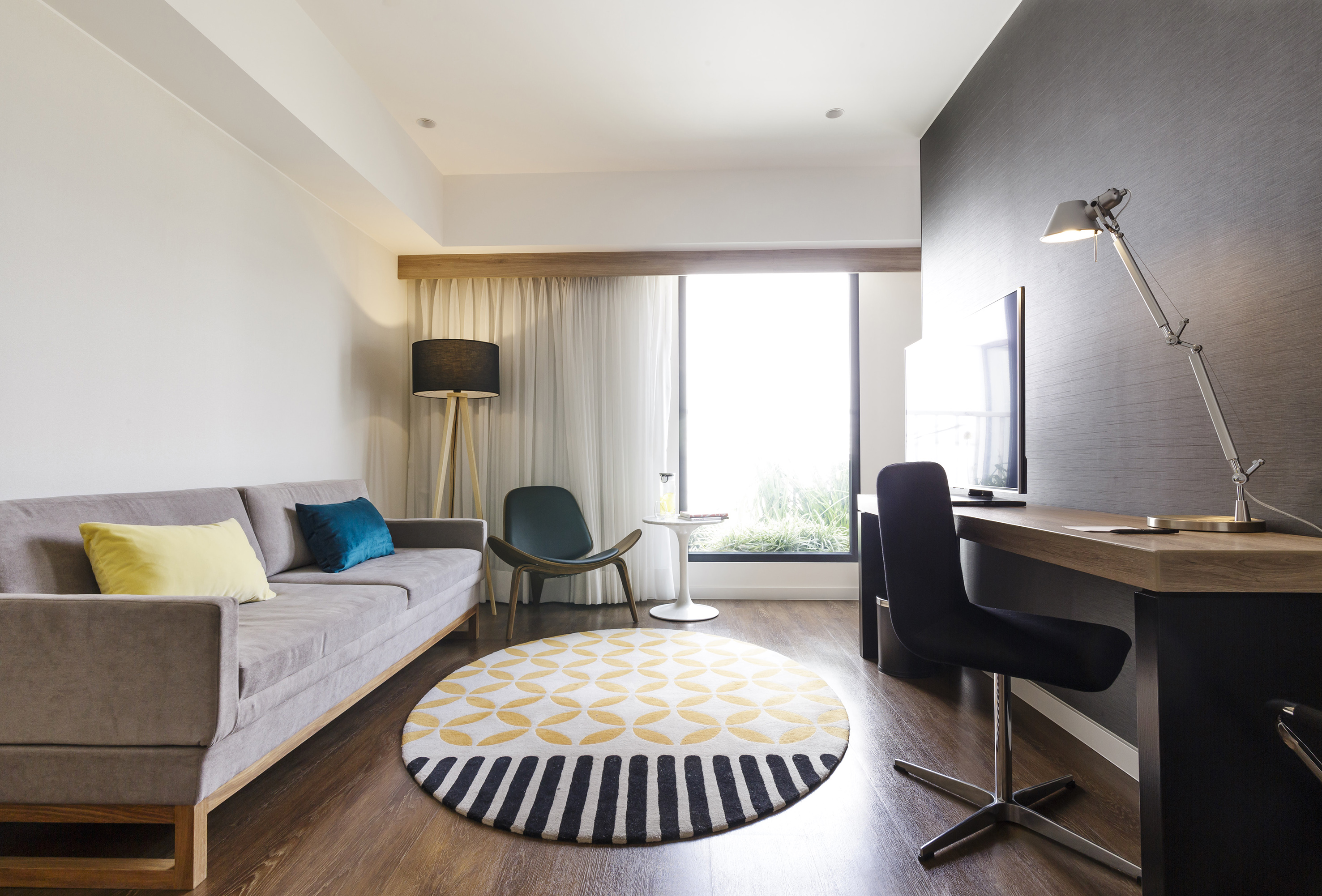 Modern living room with gray sofa, geometric rug, desk area, and large window.