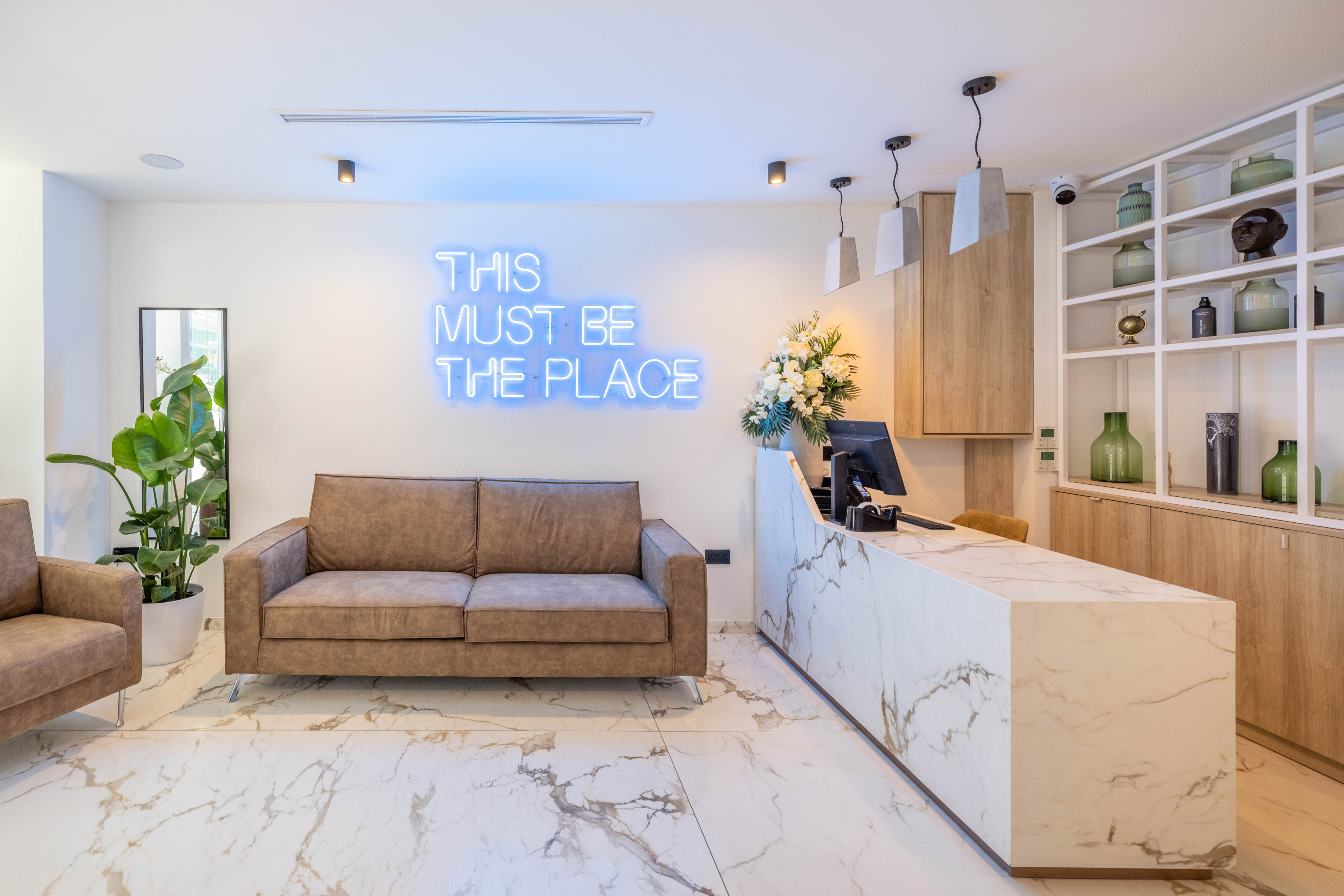 Modern hotel lobby with marble reception desk, brown sofas, and blue neon sign.