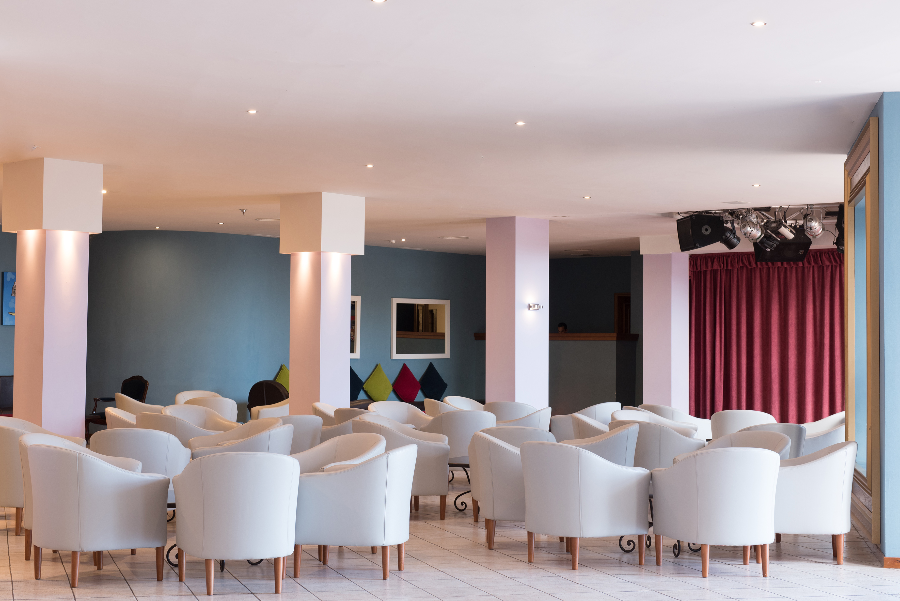 Resort lounge with white upholstered armchairs and a small stage.