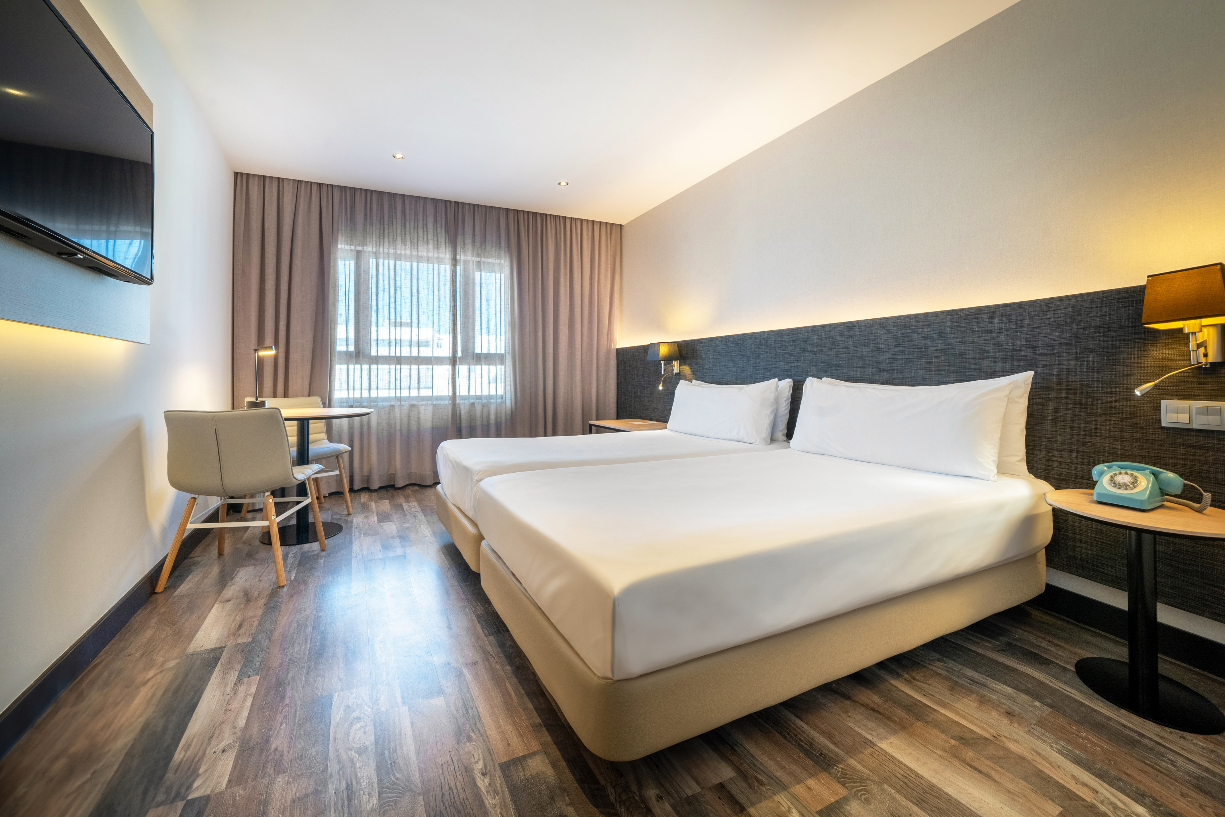 Modern hotel room with two twin beds, wood floor, TV, and a seating area.