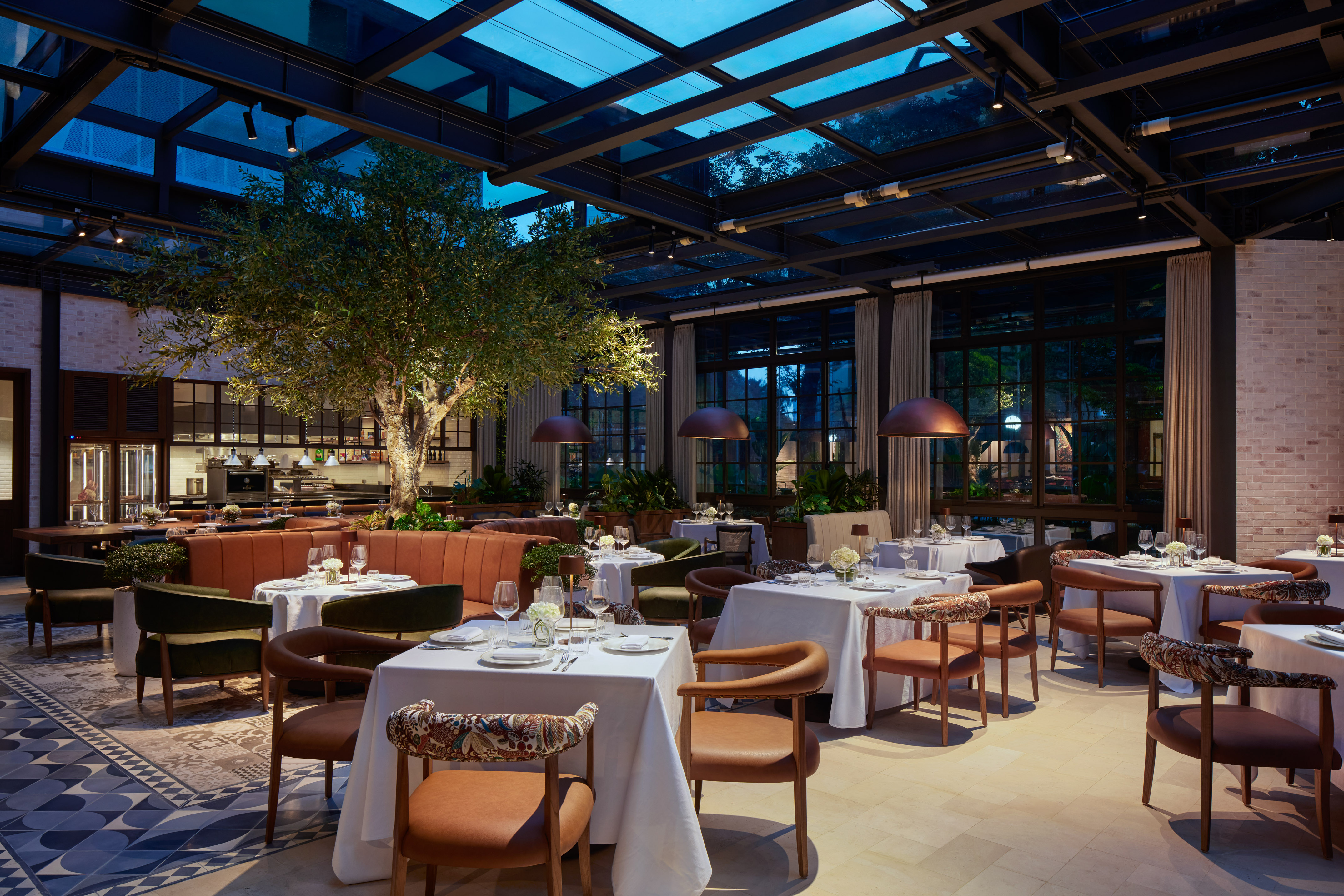 Modern luxury restaurant dining room with glass ceiling and indoor tree.