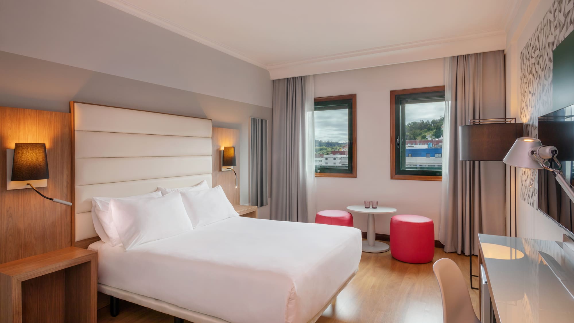 Contemporary hotel room with king-size bed, work desk, and city view.