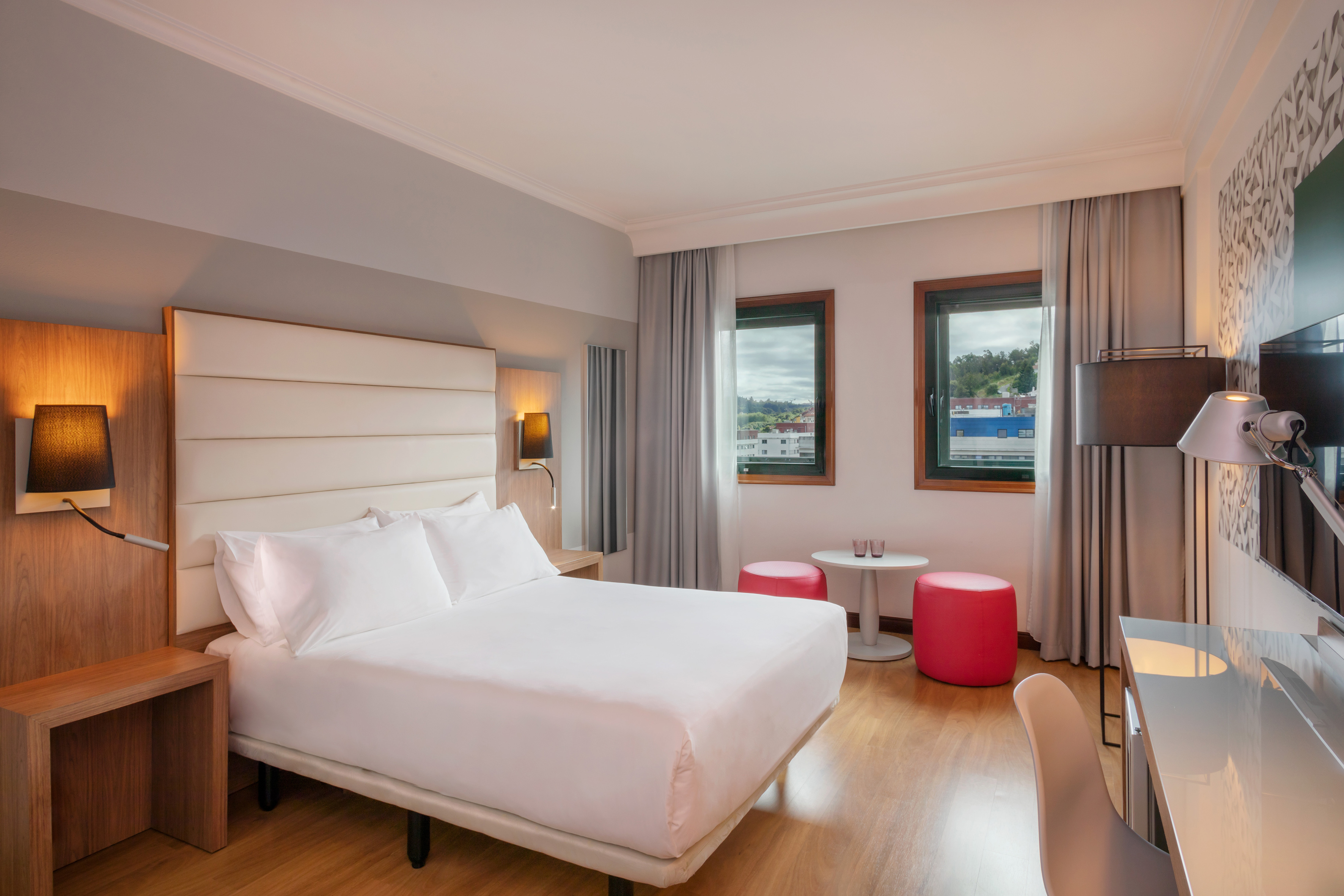 Contemporary hotel room with king-size bed, work desk, and city view.