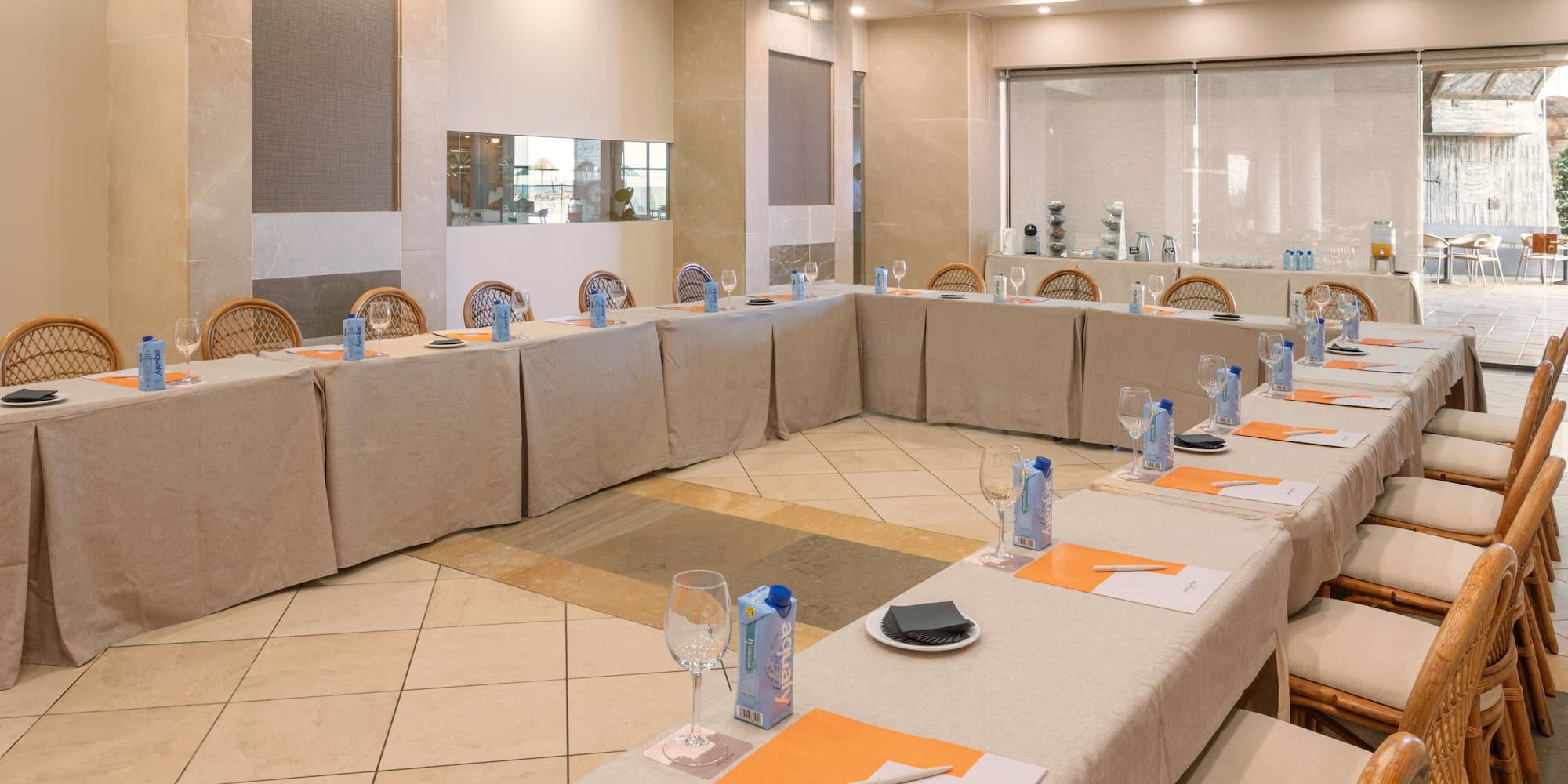 Conference room with U-shape setup, tables, rattan chairs, and refreshments.
