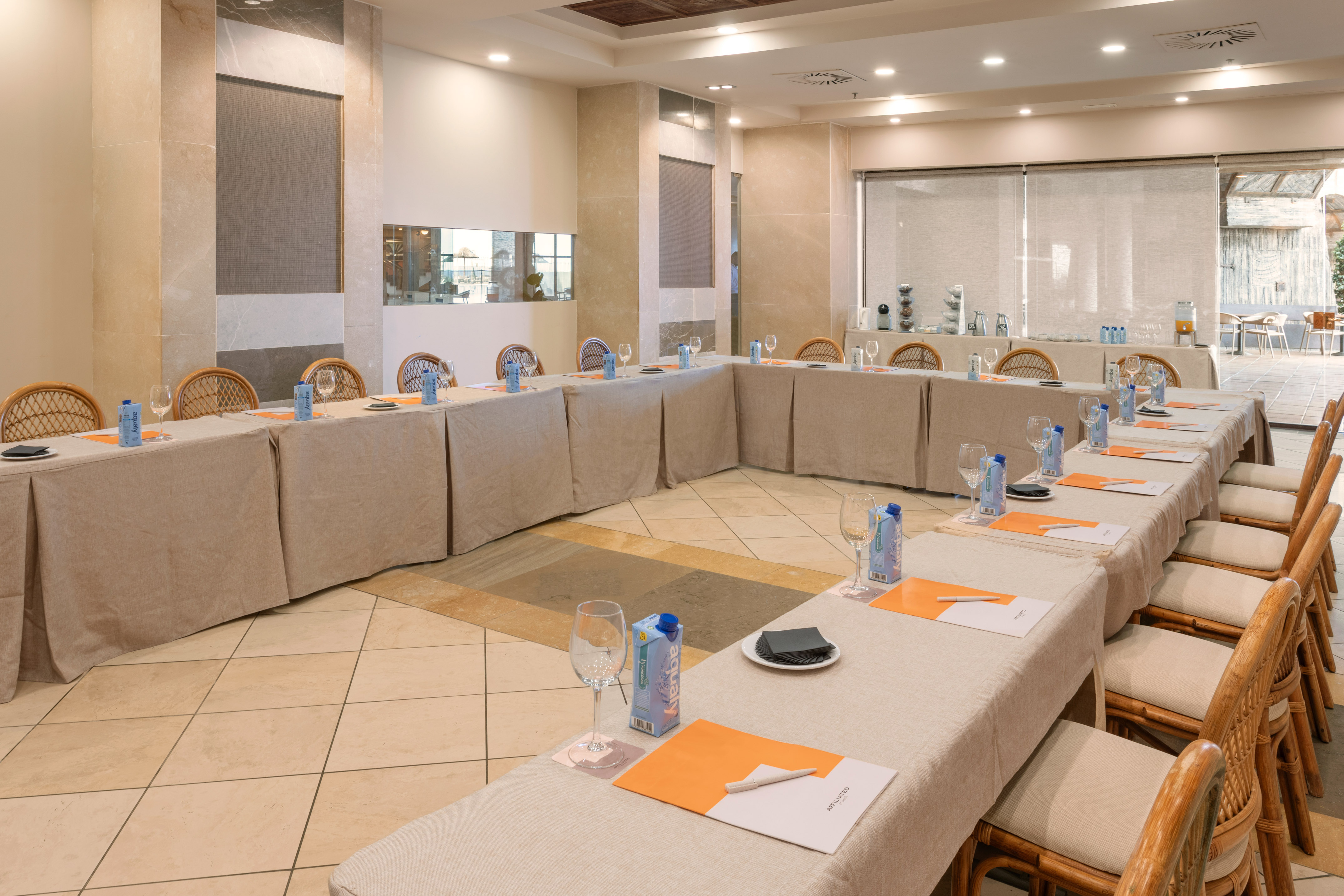 Conference room with U-shape setup, tables, rattan chairs, and refreshments.