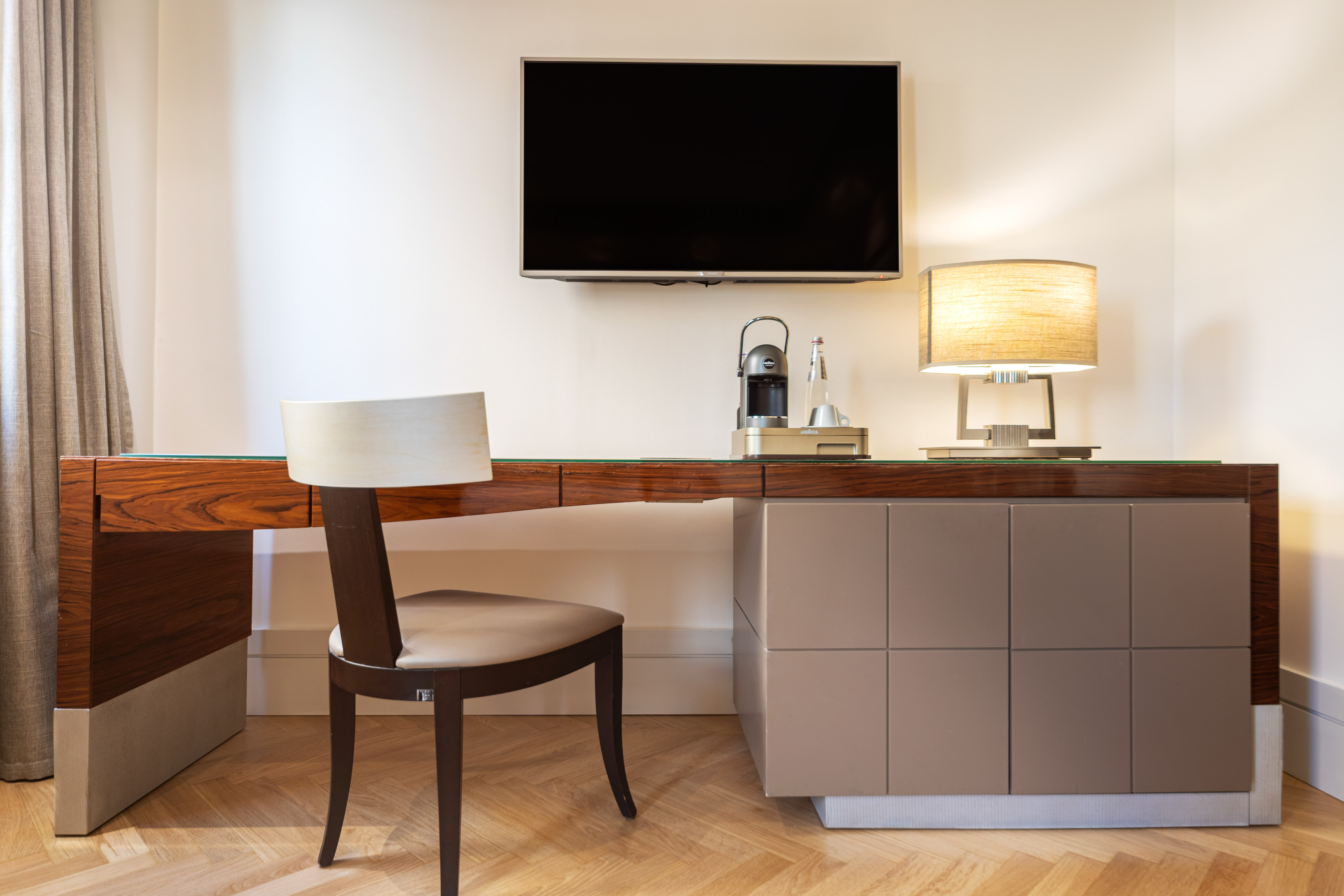 Modern hotel room desk with wall-mounted TV, coffee machine, and lamp.