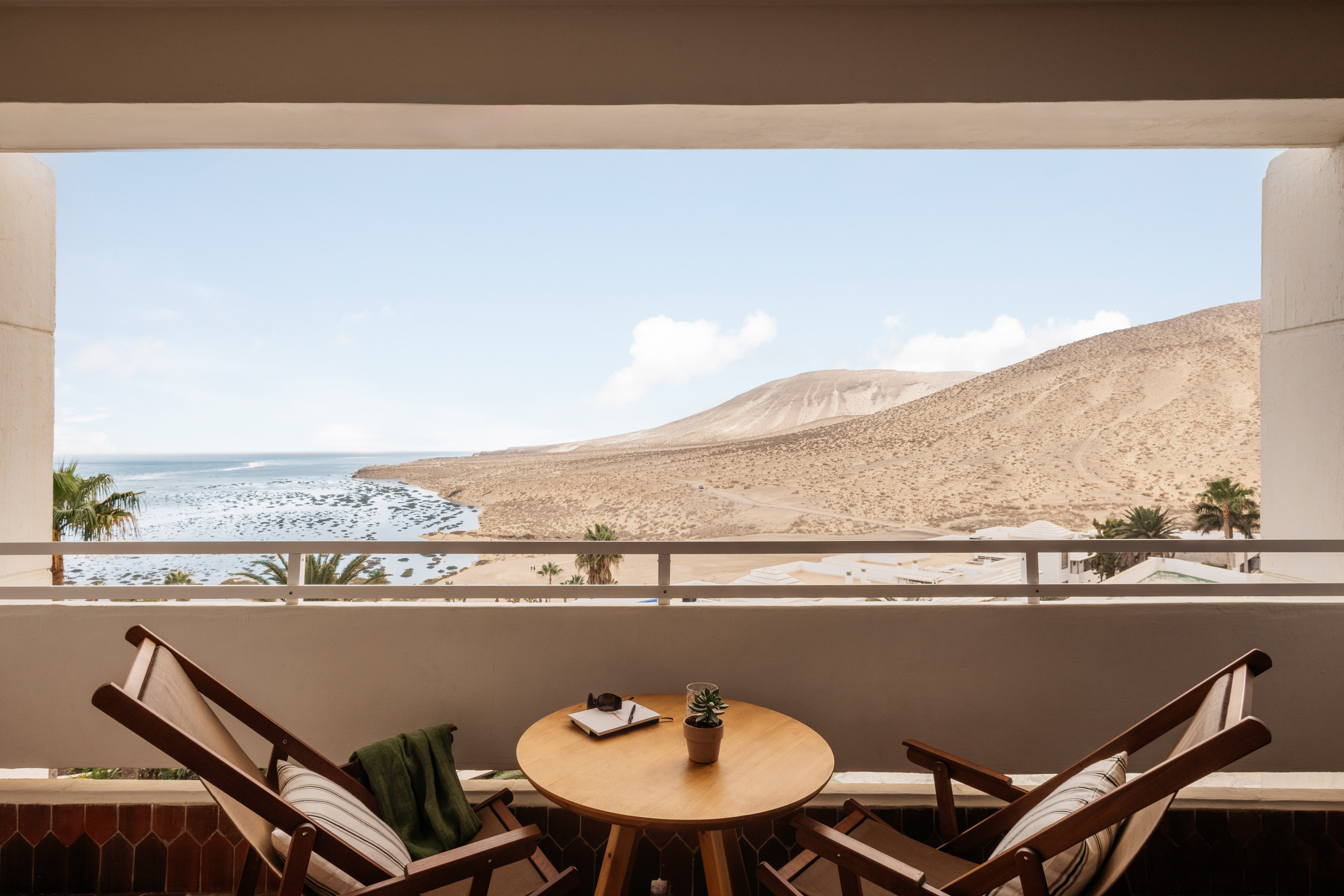 Balcony with lounge chairs, ocean view, and arid desert hills.