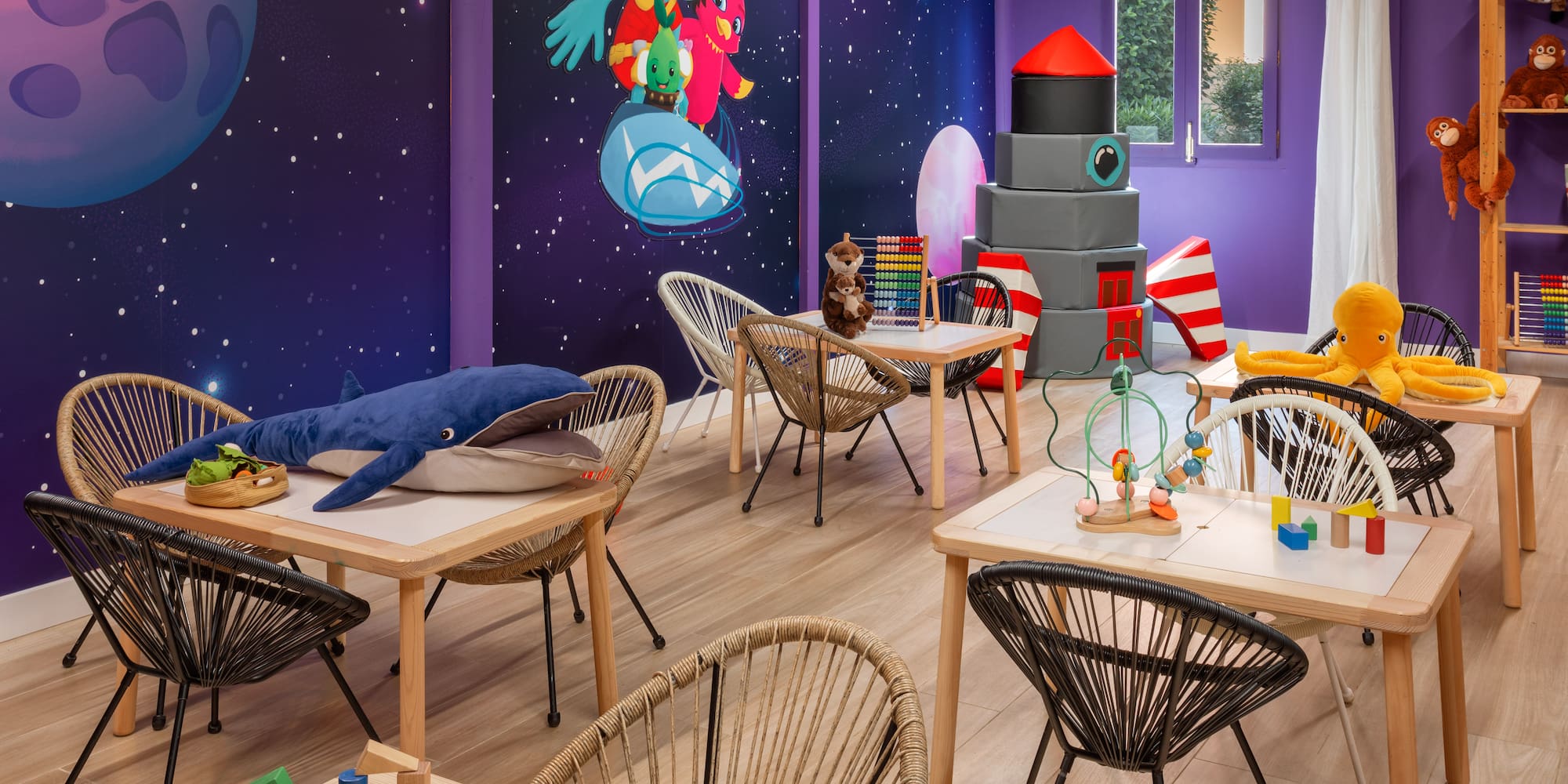 Vibrant space-themed kids' playroom with activity tables, chairs, and toys.