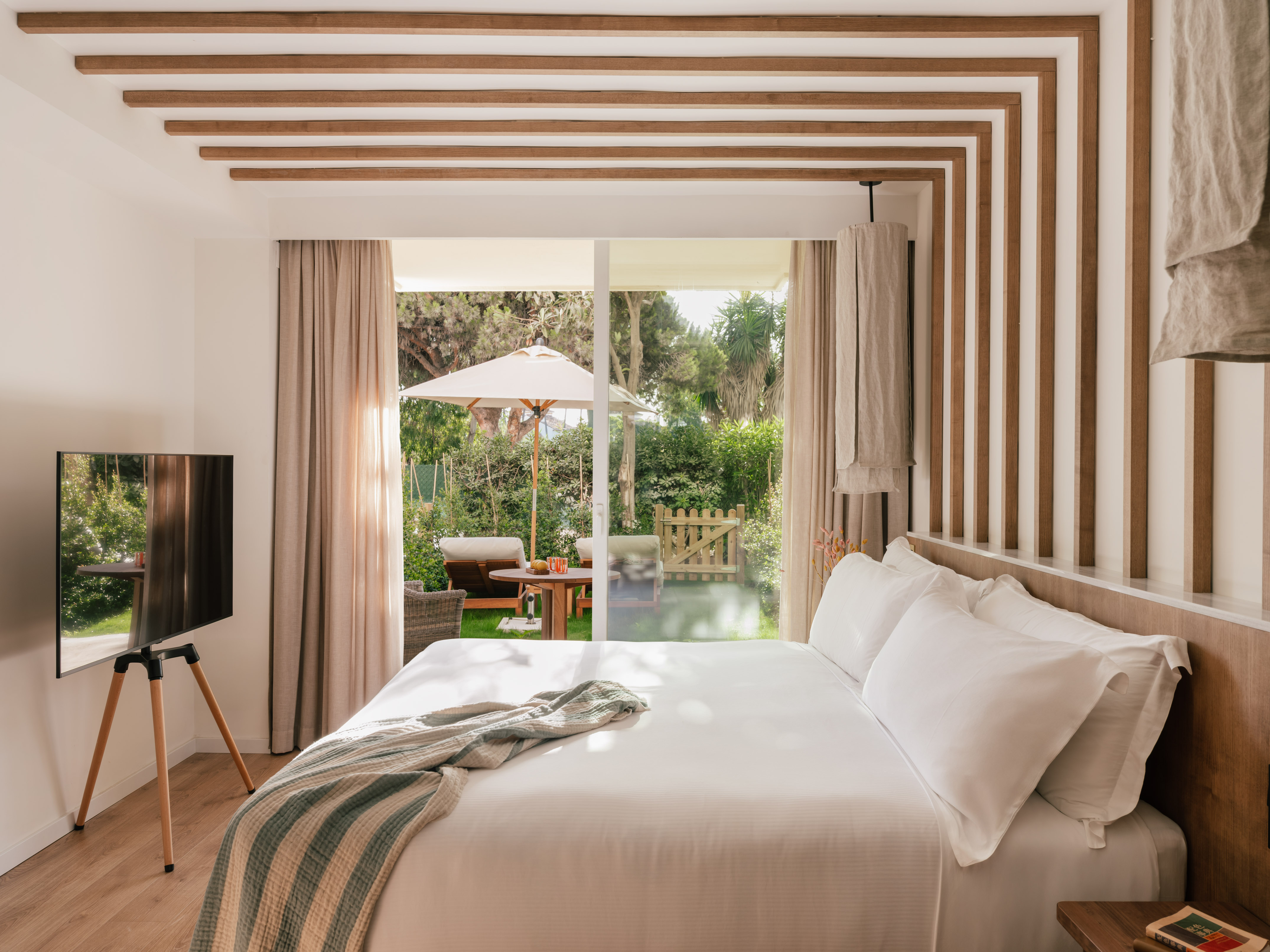 Modern bedroom with garden view, white bed, and natural wood decor.