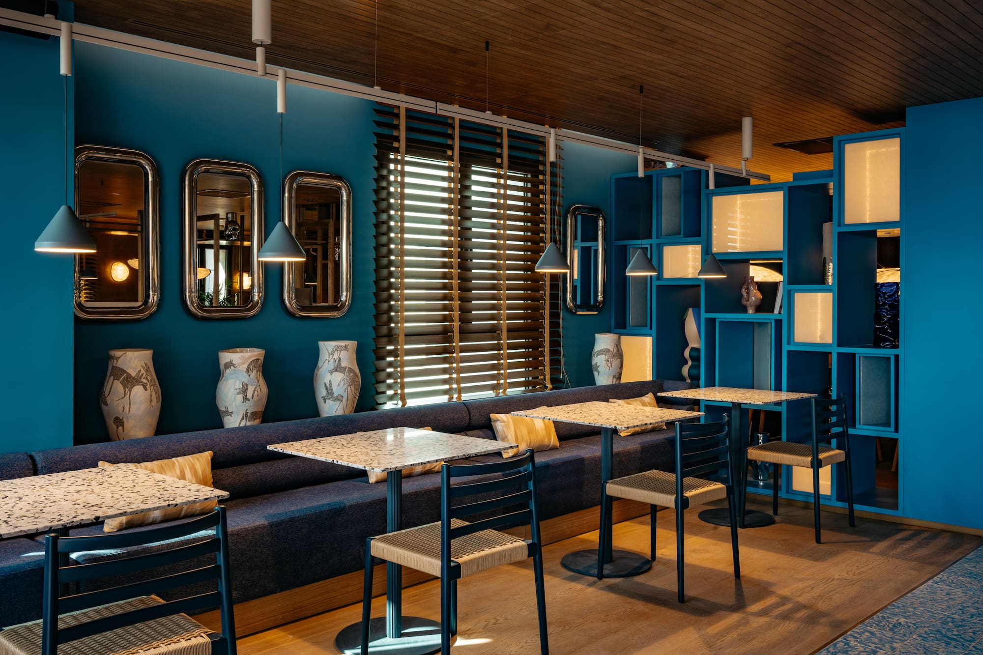 Vibrant blue restaurant with terrazzo tables, banquette seating, and mirrors.