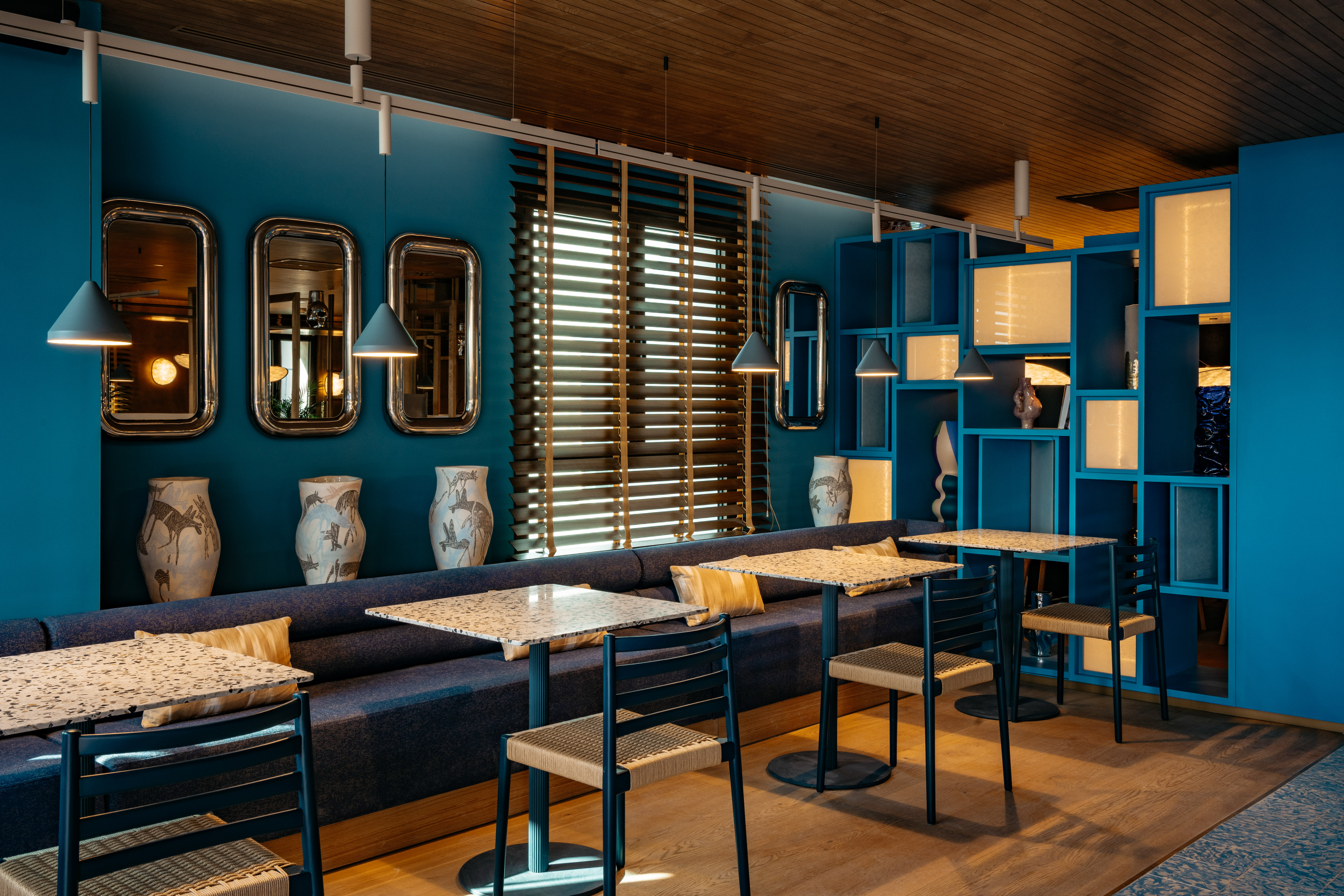 Vibrant blue restaurant with terrazzo tables, banquette seating, and mirrors.