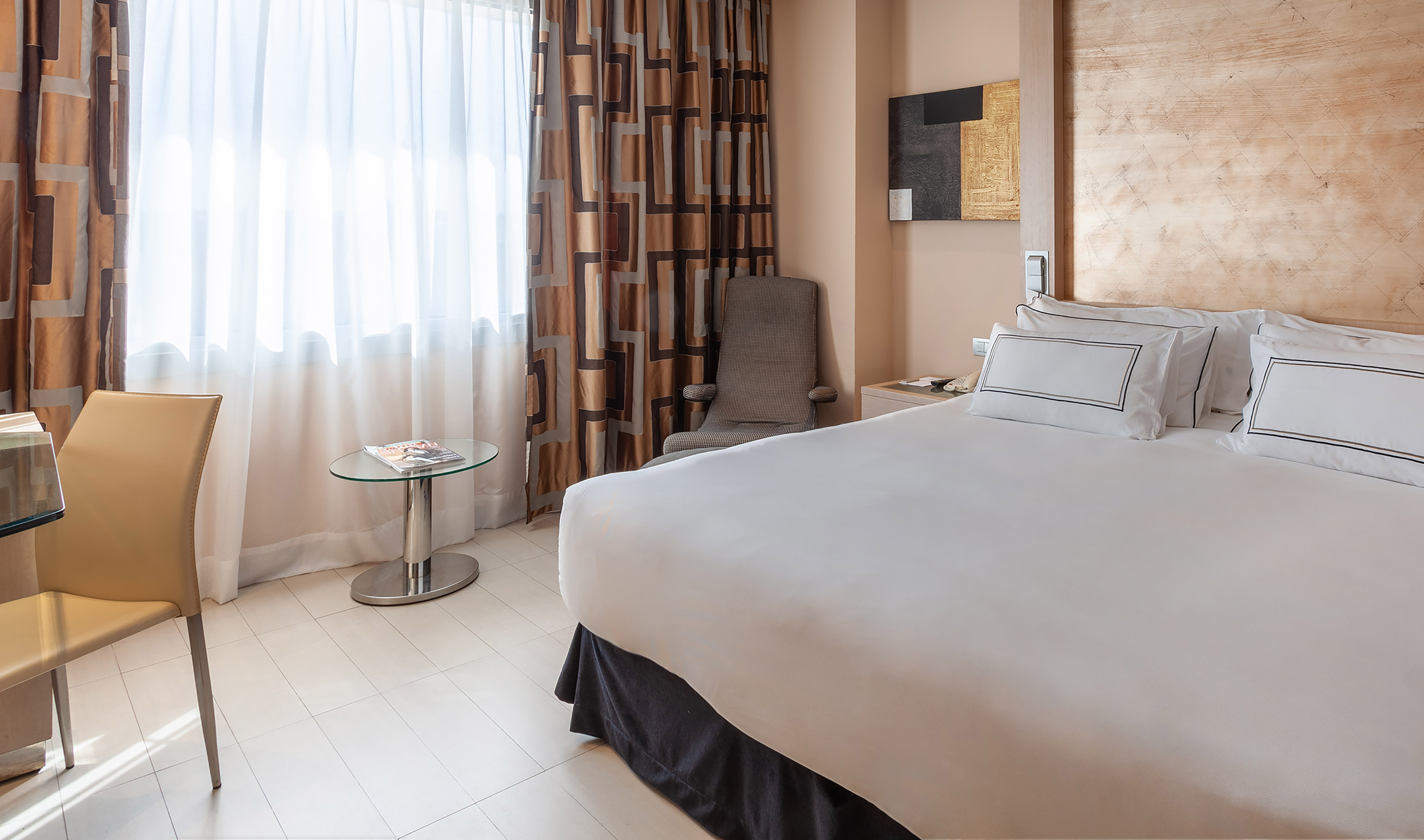 Modern hotel room with king bed, patterned curtains, and sitting area.