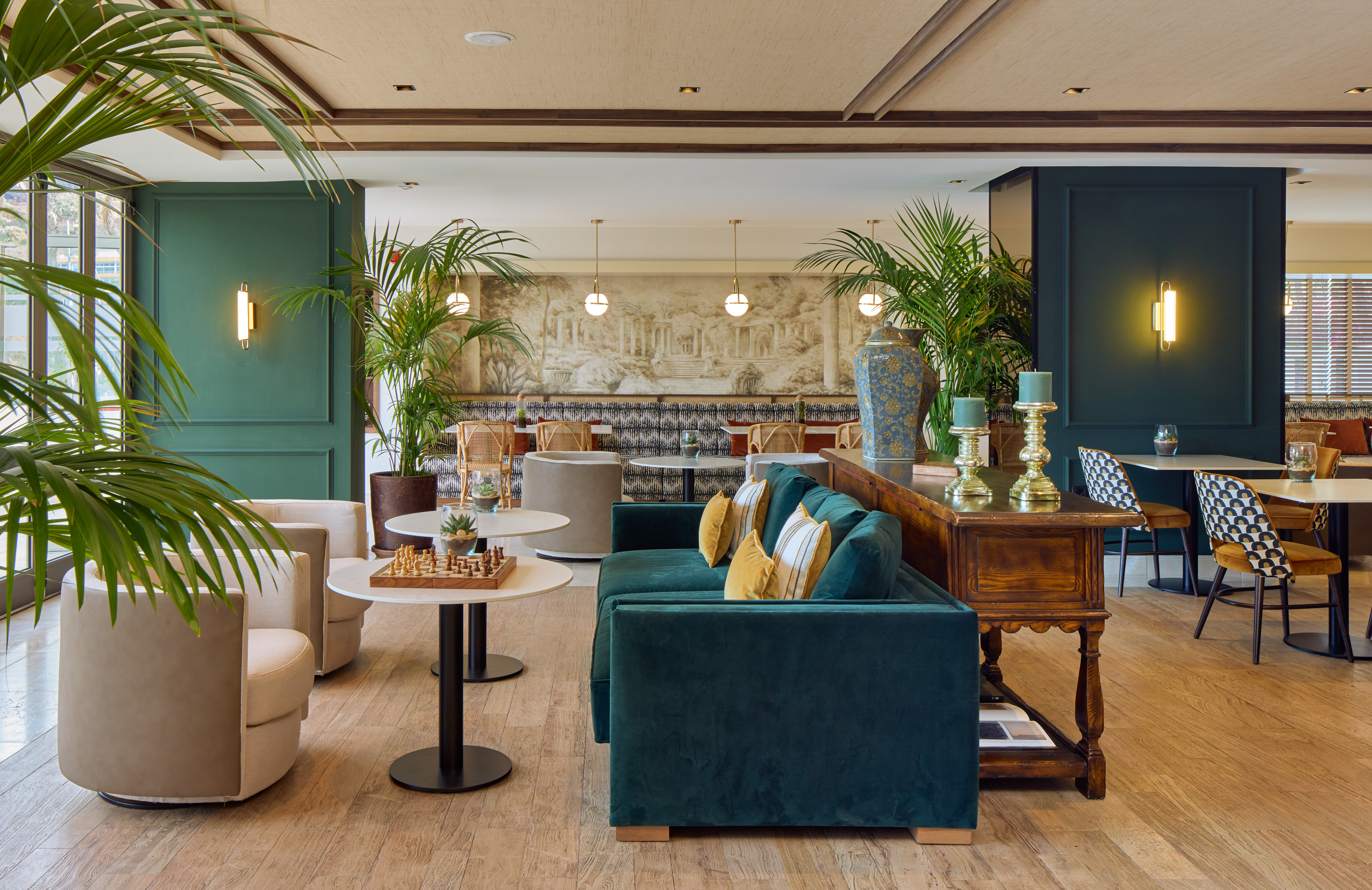 Elegant hotel lounge with green velvet sofa, beige armchairs, and lush palm plants.