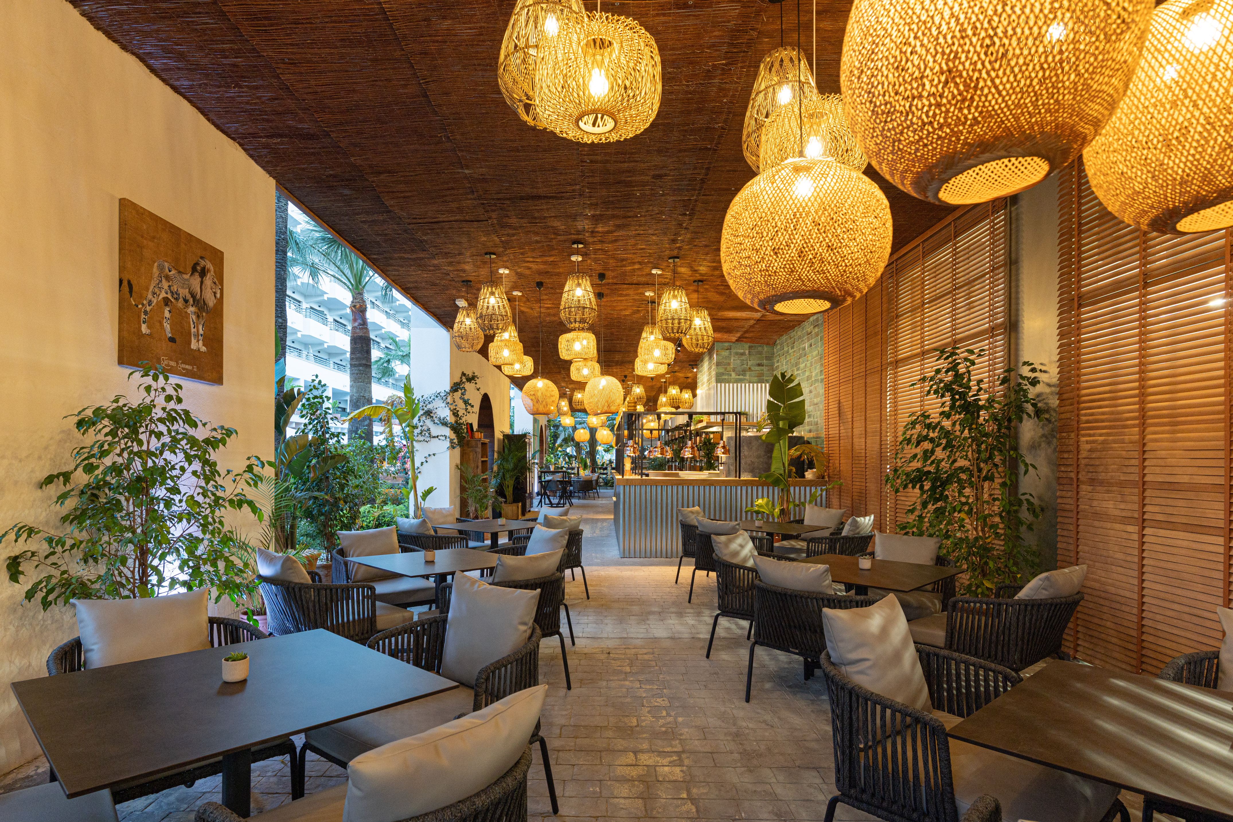 Hotel restaurant terrace with modern seating, woven lights, and tropical plants.