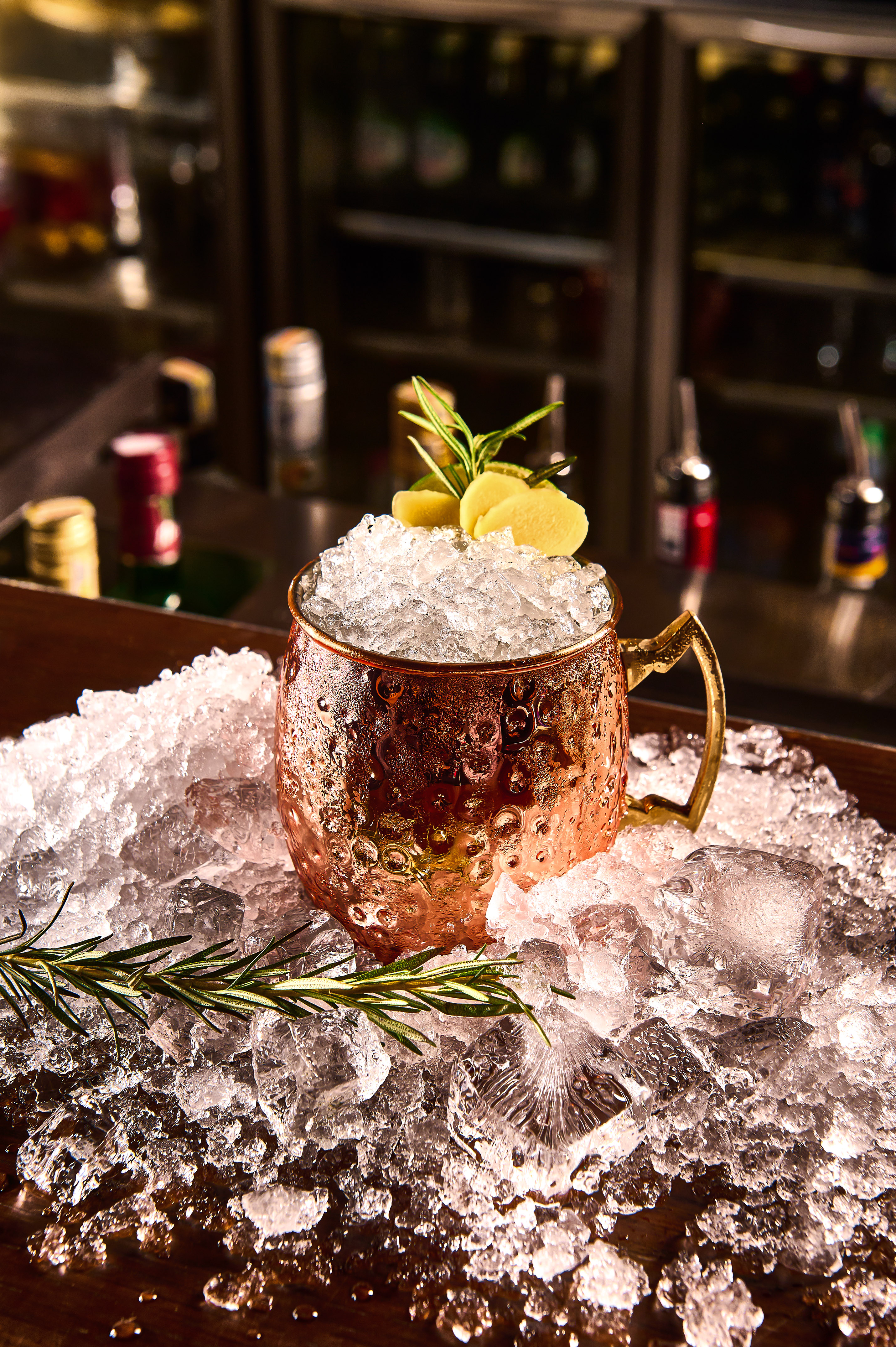 Moscow Mule cocktail in copper mug with ginger, rosemary, and crushed ice at a bar.