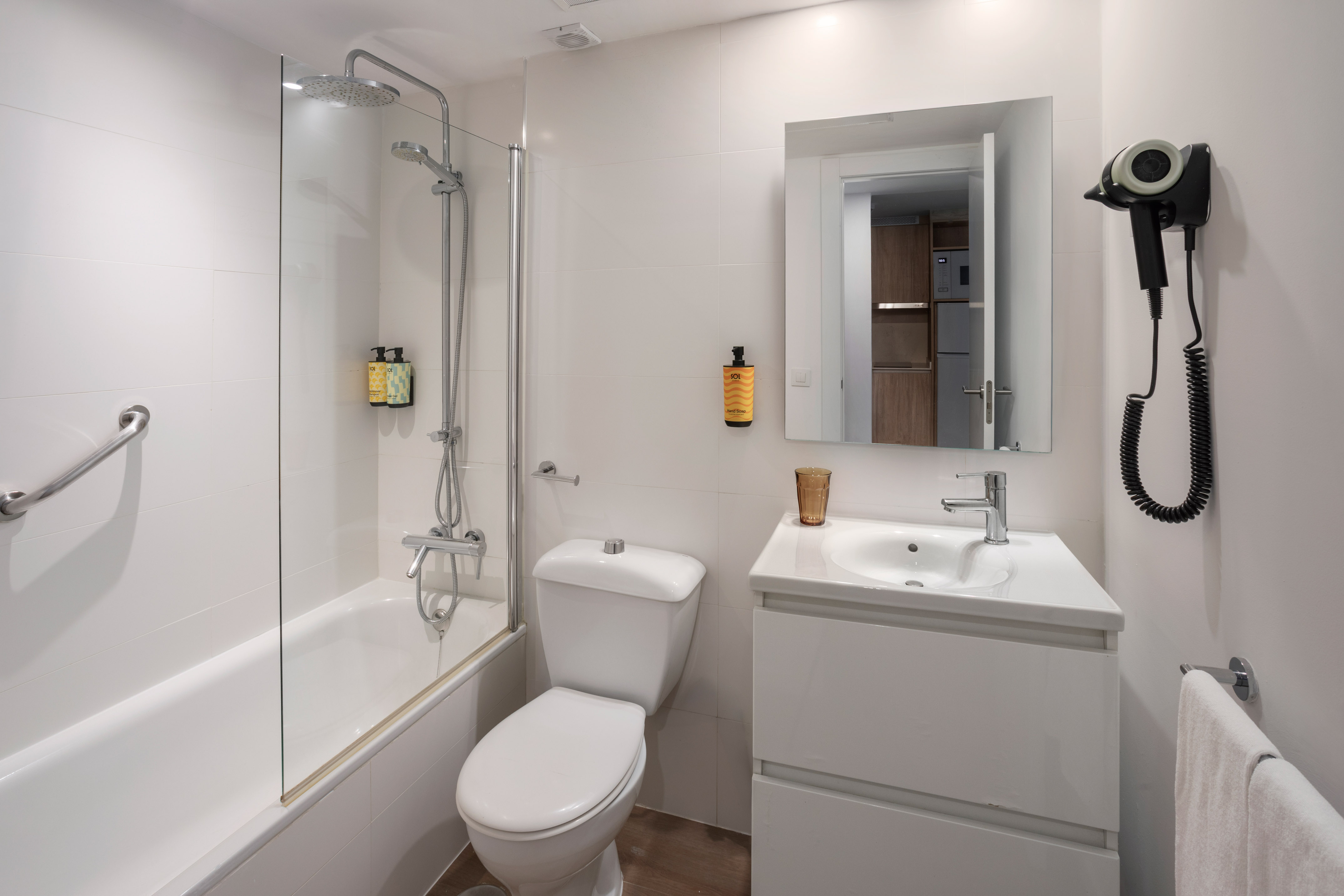 Baño de hotel blanco con bañera, ducha, inodoro, lavabo y secador.