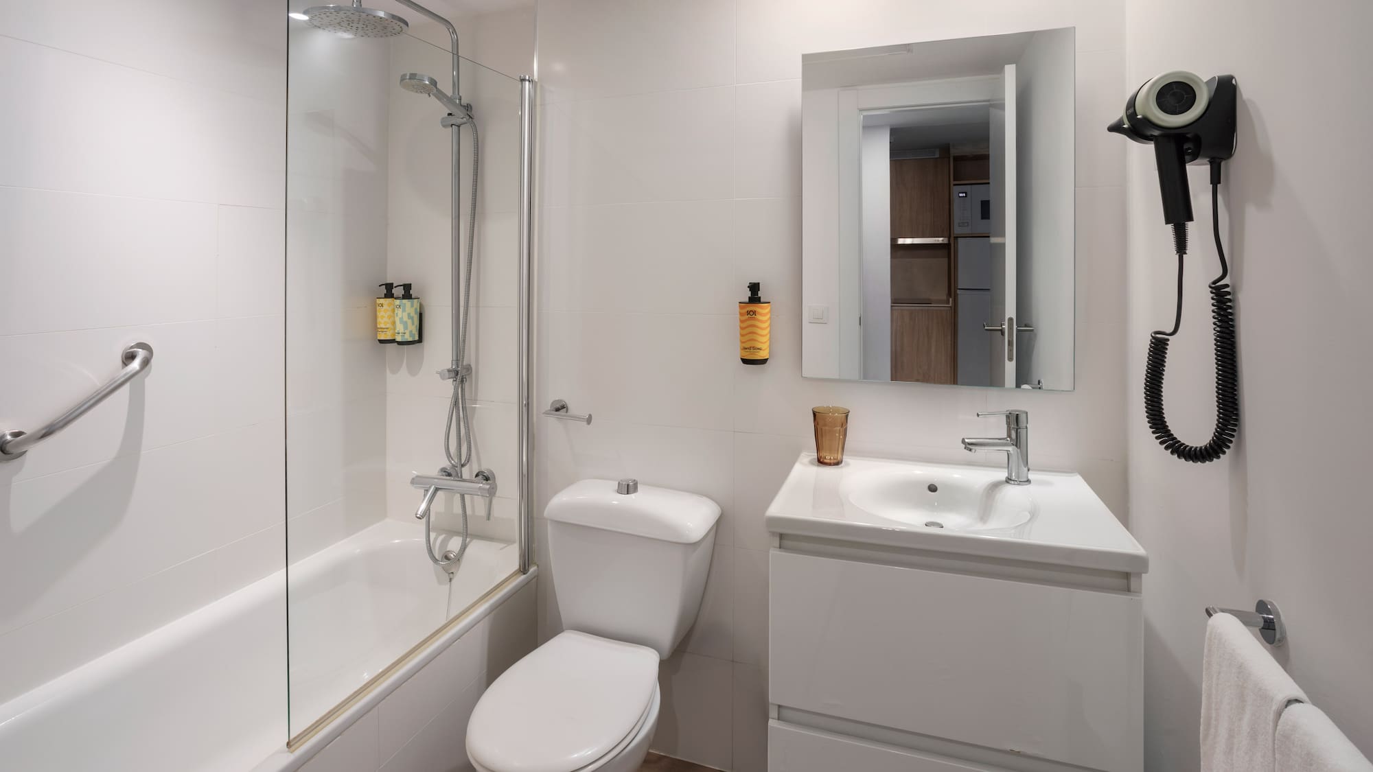Baño de hotel blanco con bañera, ducha, inodoro, lavabo y secador.