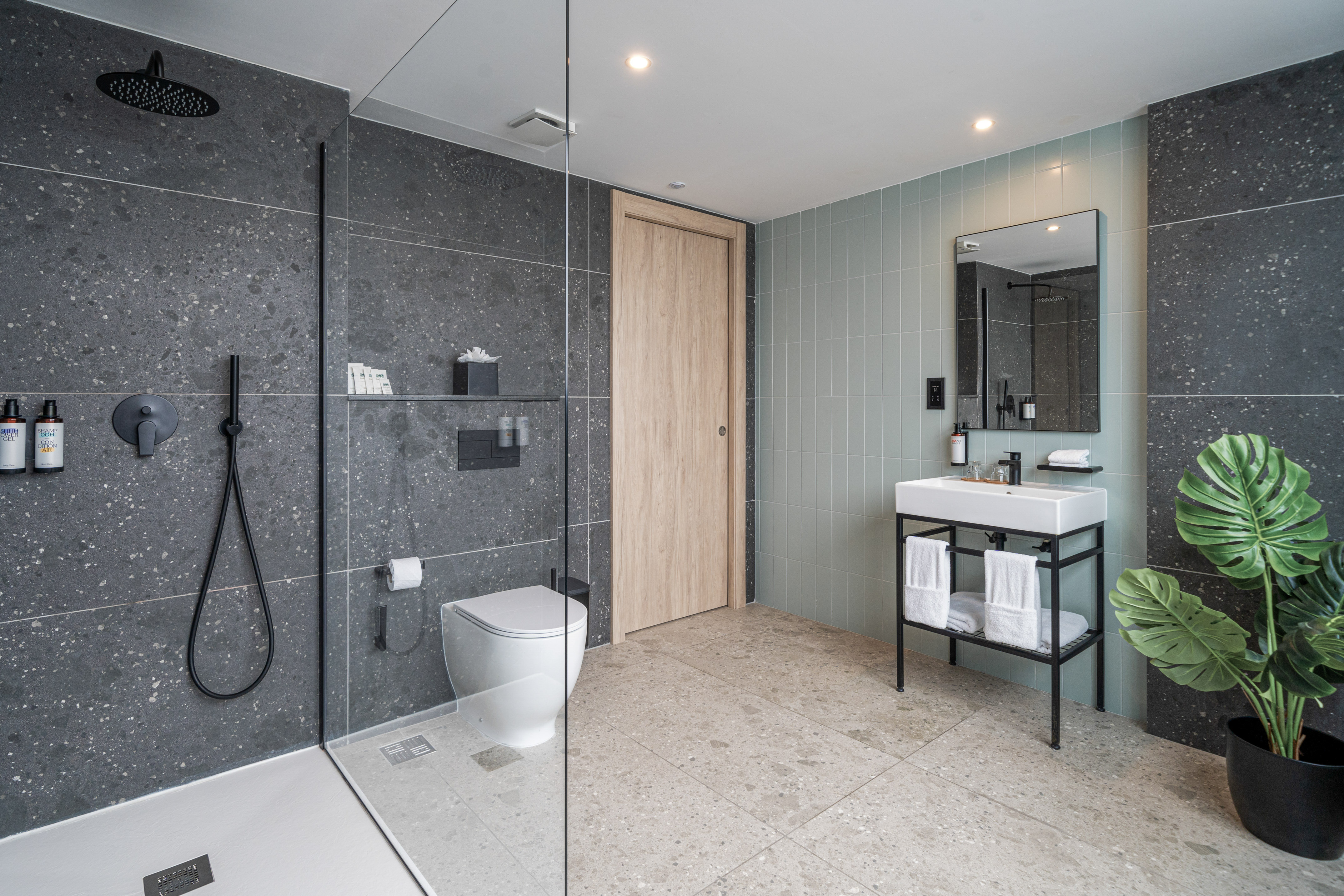 Contemporary bathroom with dark grey shower, white toilet, mint green wall, and vanity.