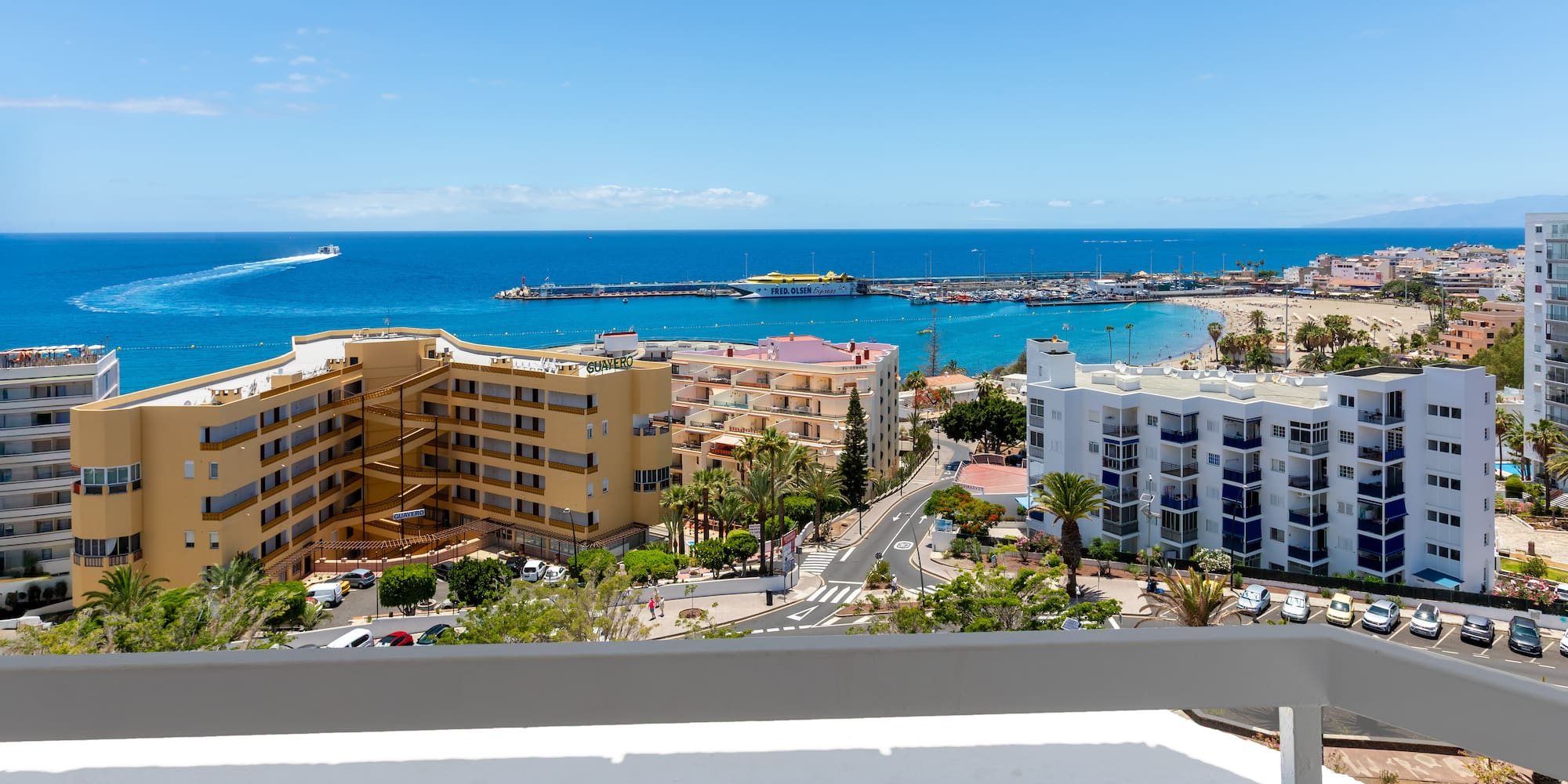 Coastal resort ocean view with sandy beach, marina, hotels, and blue sky.