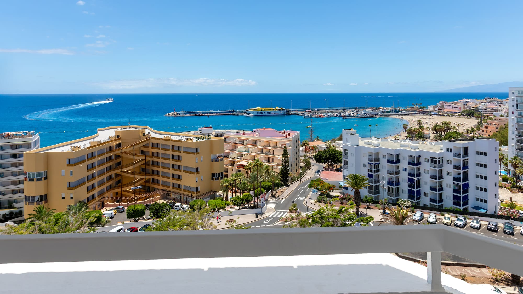 Coastal resort ocean view with sandy beach, marina, hotels, and blue sky.