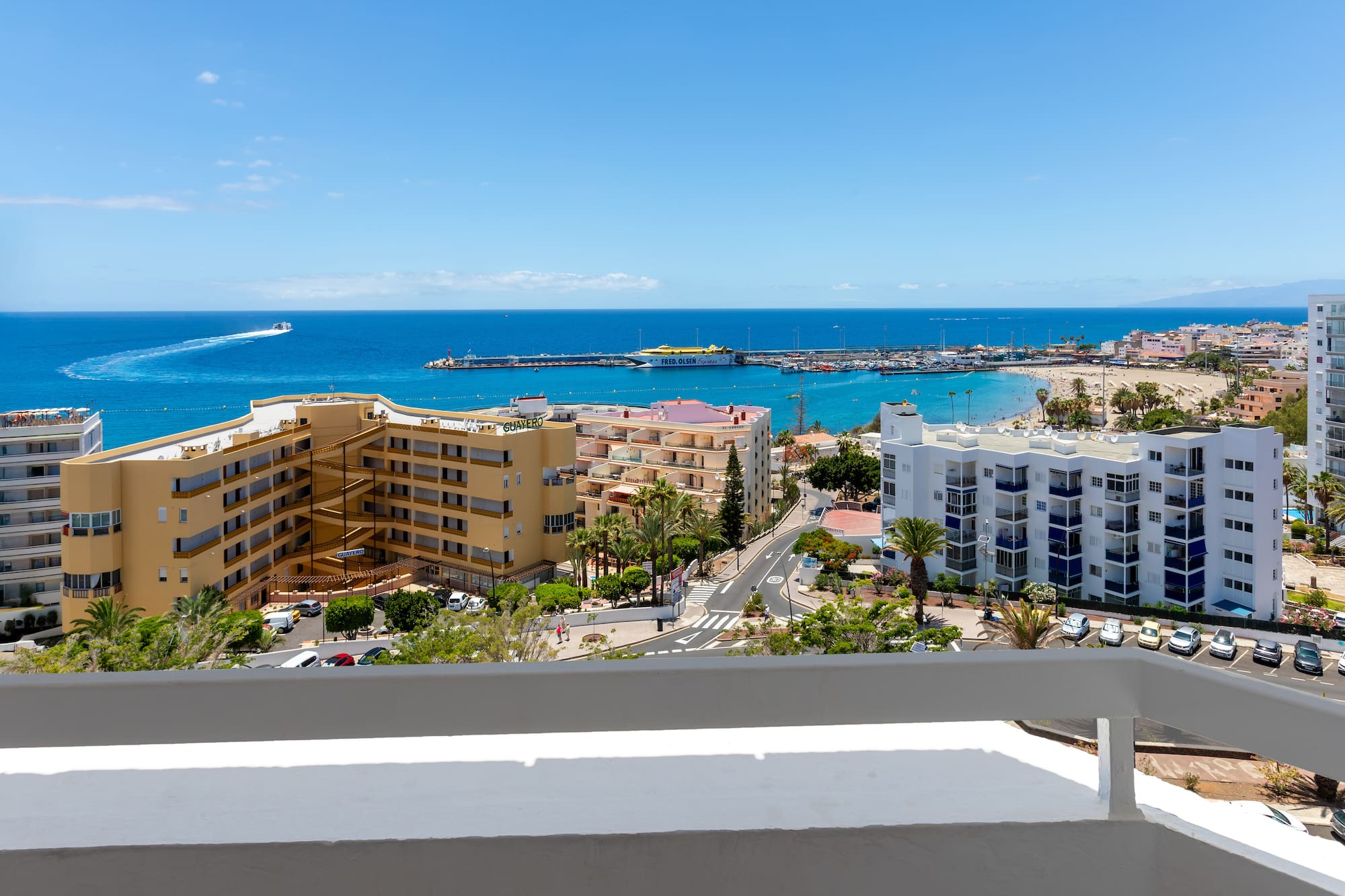 Coastal resort ocean view with sandy beach, marina, hotels, and blue sky.