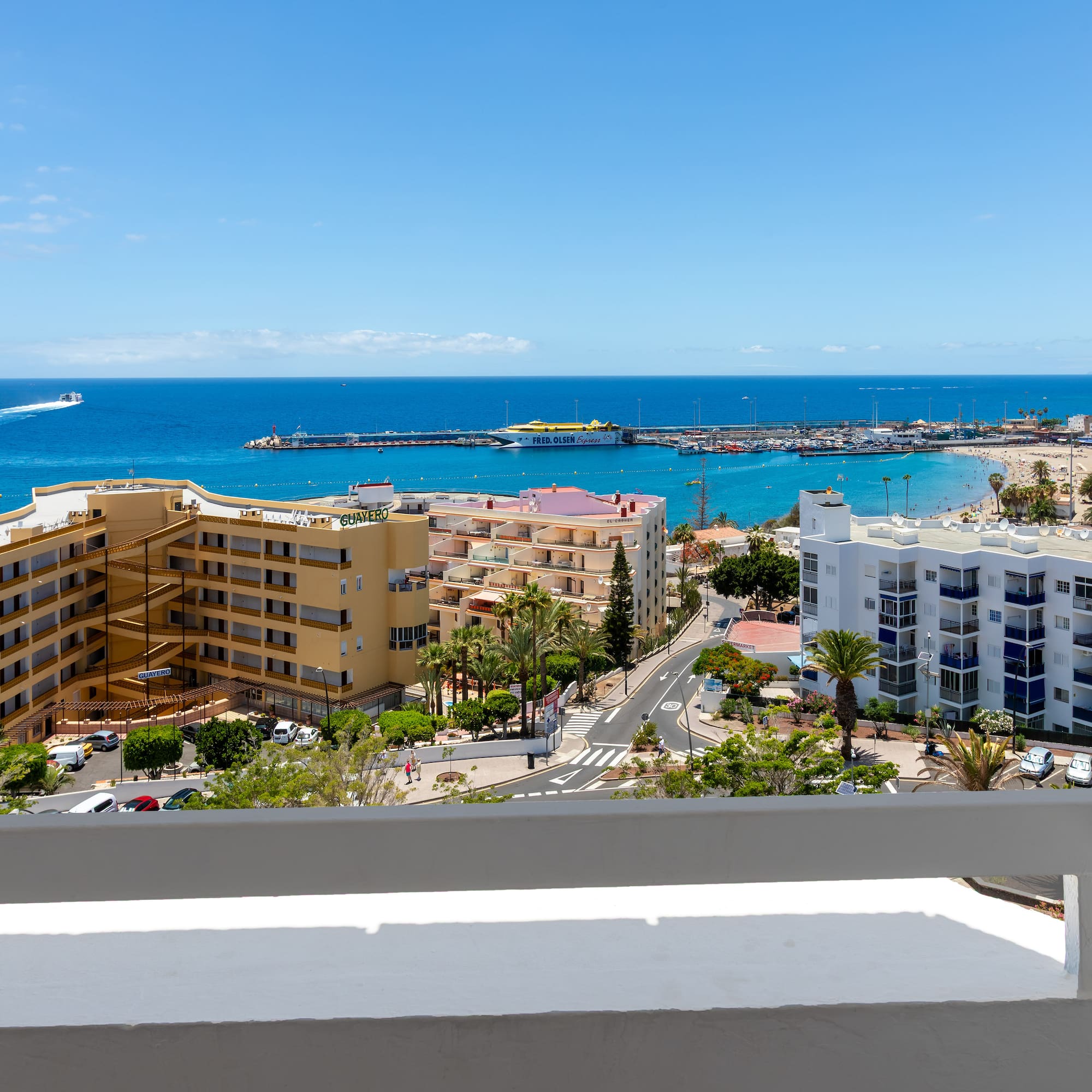 Coastal resort ocean view with sandy beach, marina, hotels, and blue sky.