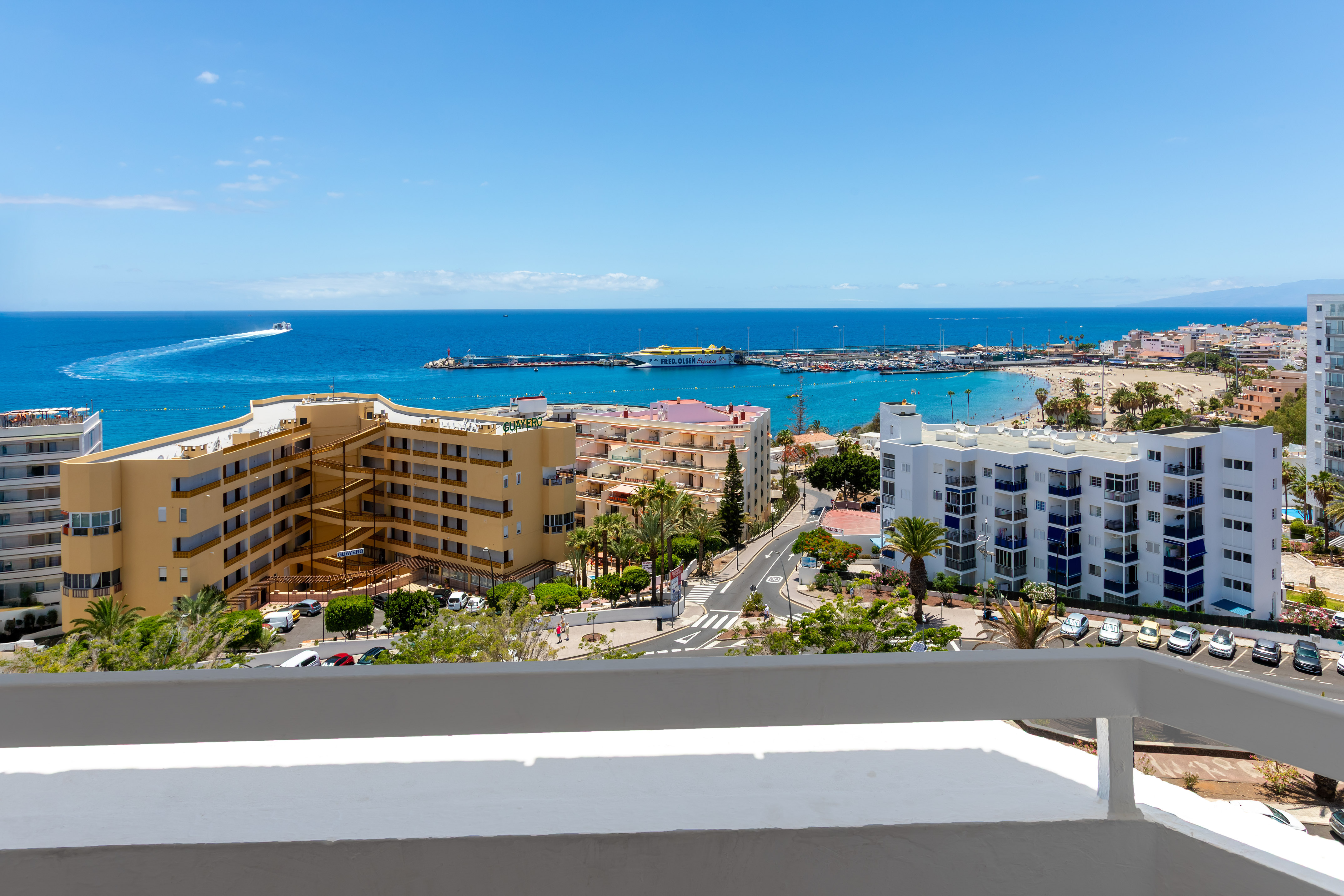 Coastal resort ocean view with sandy beach, marina, hotels, and blue sky.