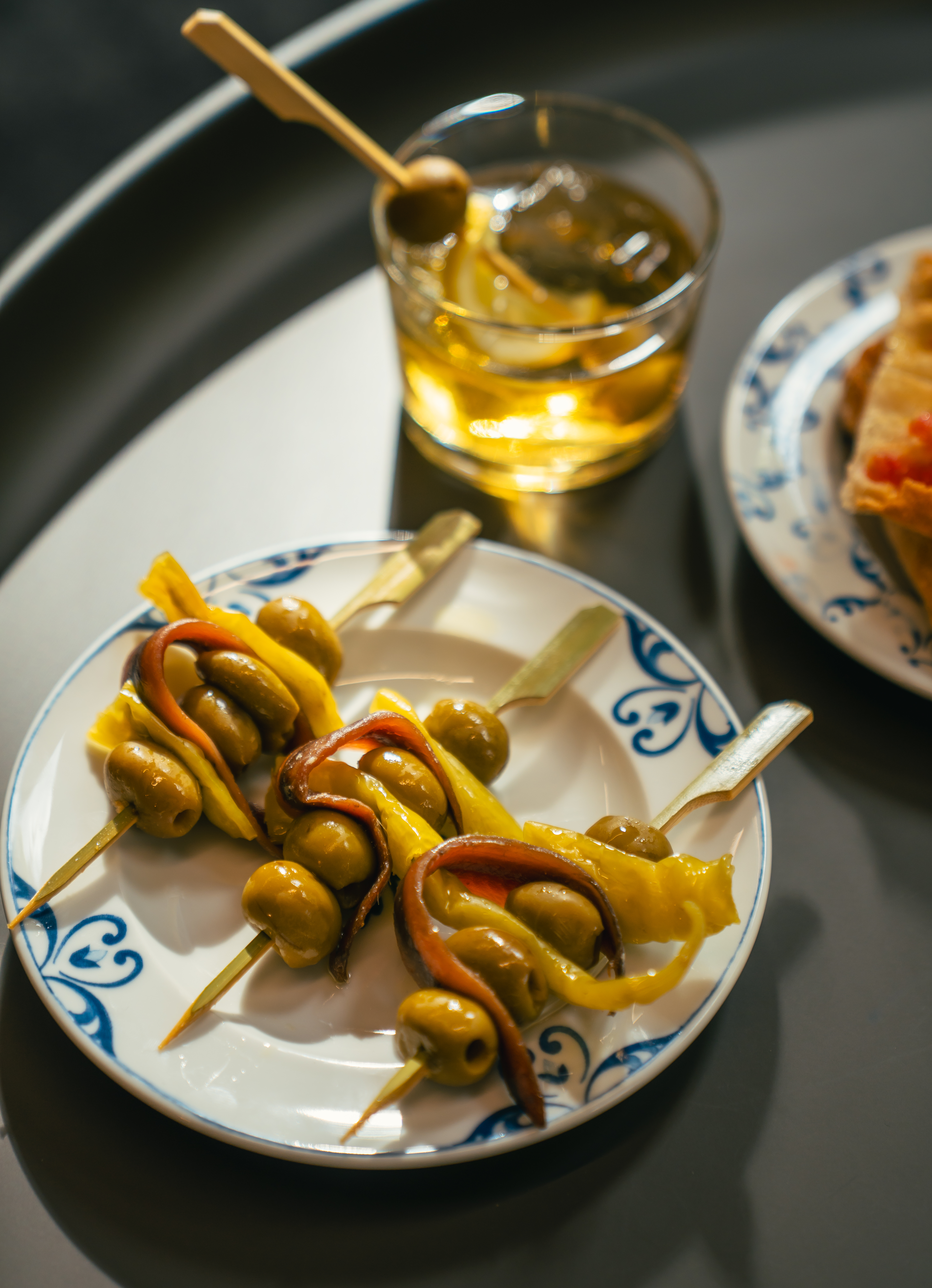 Gilda skewers of olives, anchovies, peppers, beside a cocktail.