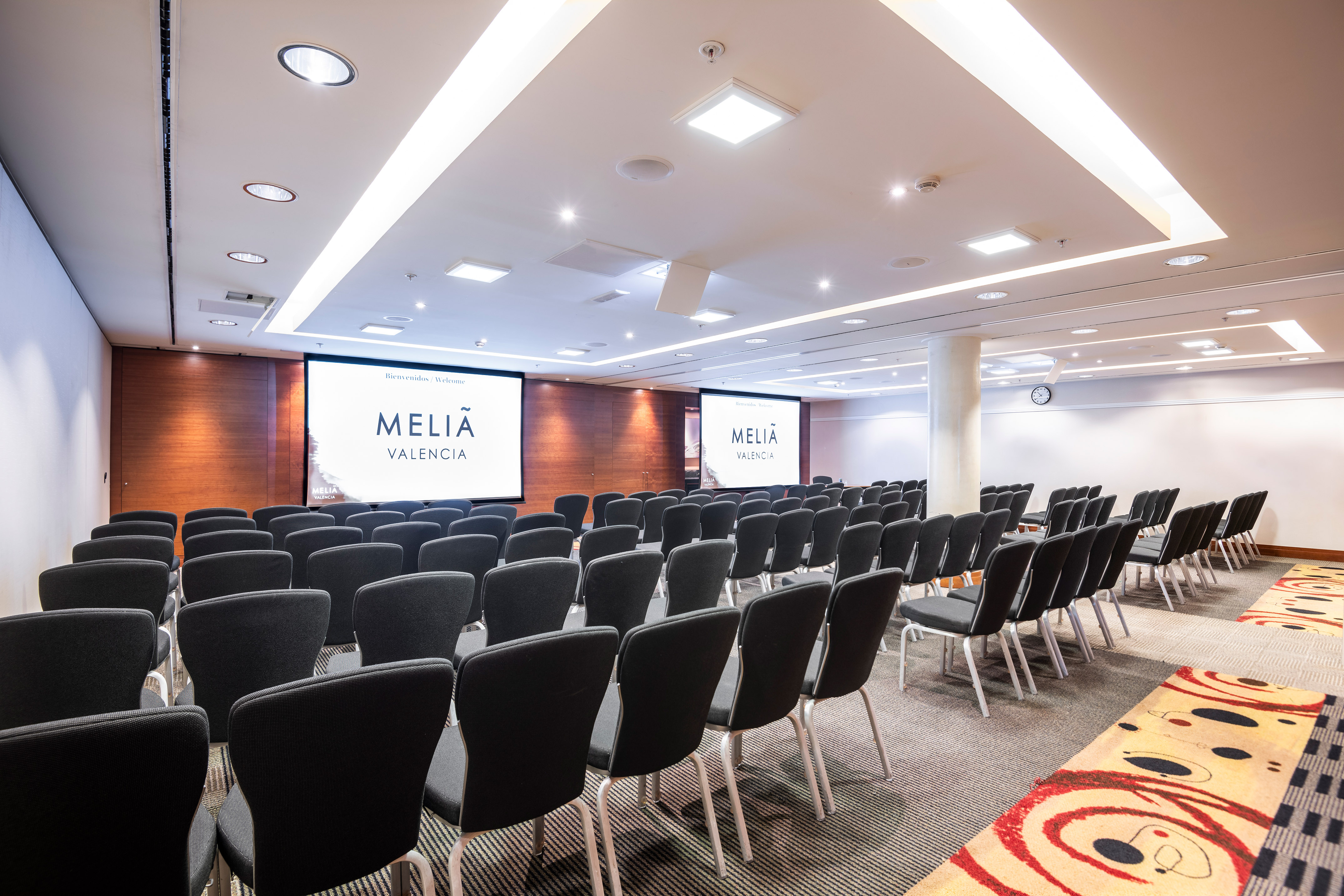 Meliá Valencia conference room with rows of chairs and dual screens for presentations.