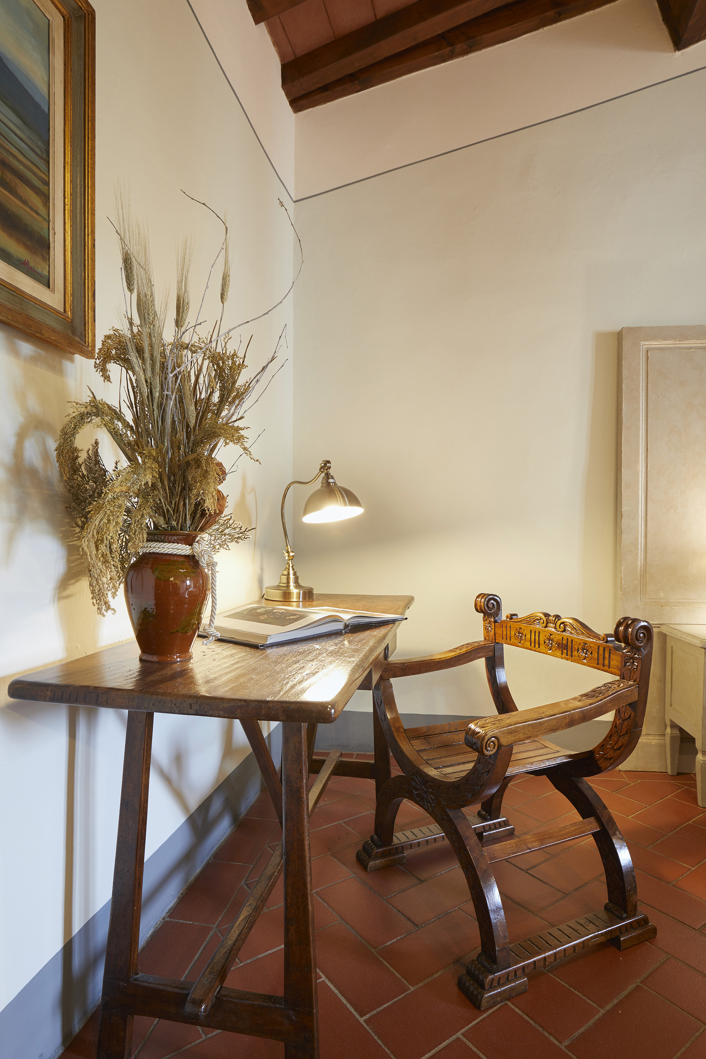 Rustic wooden desk with ornate carved chair, lamp, and dried flowers.