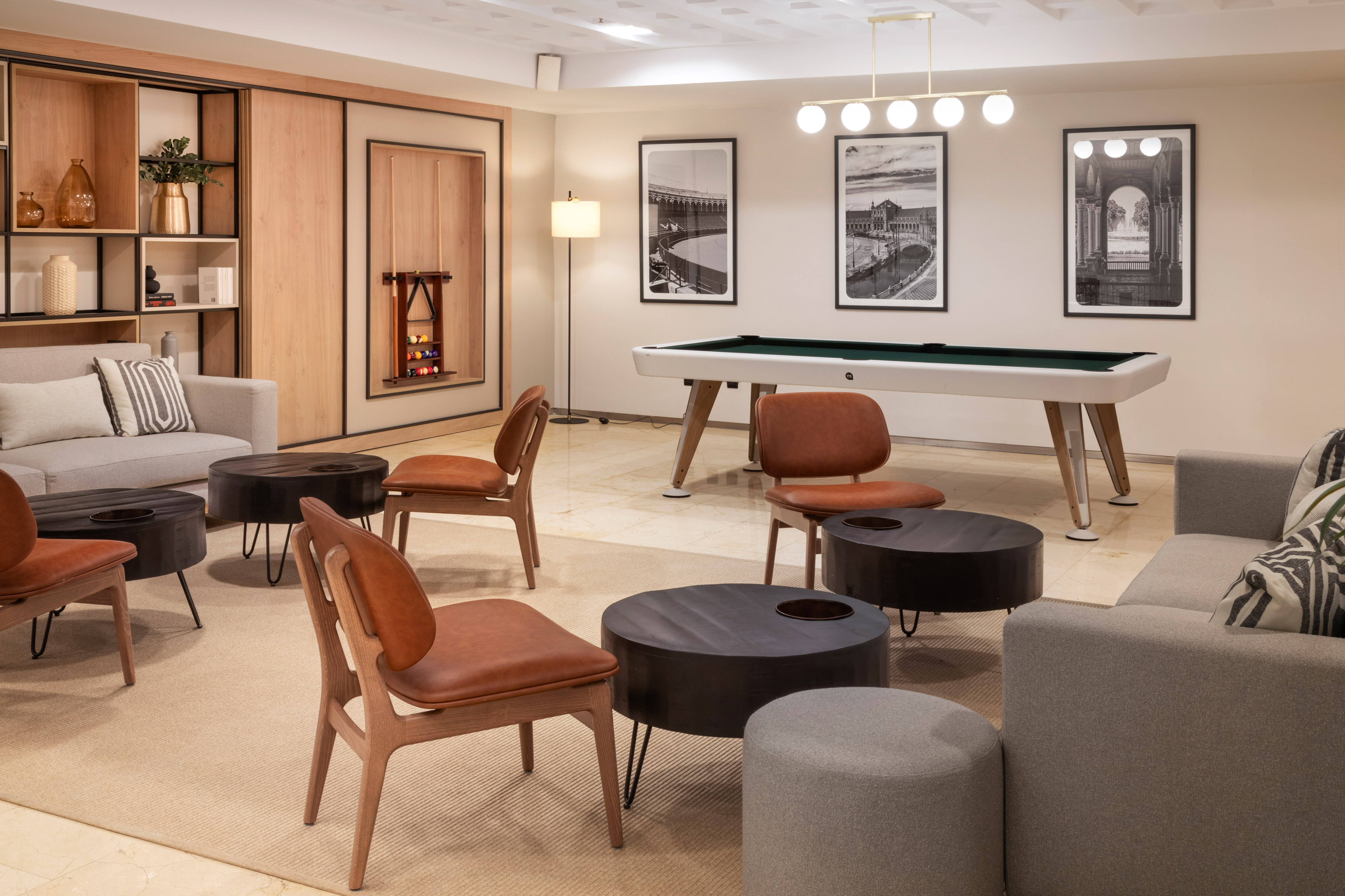 Modern lounge with a pool table, grey sofas, and brown leather chairs.