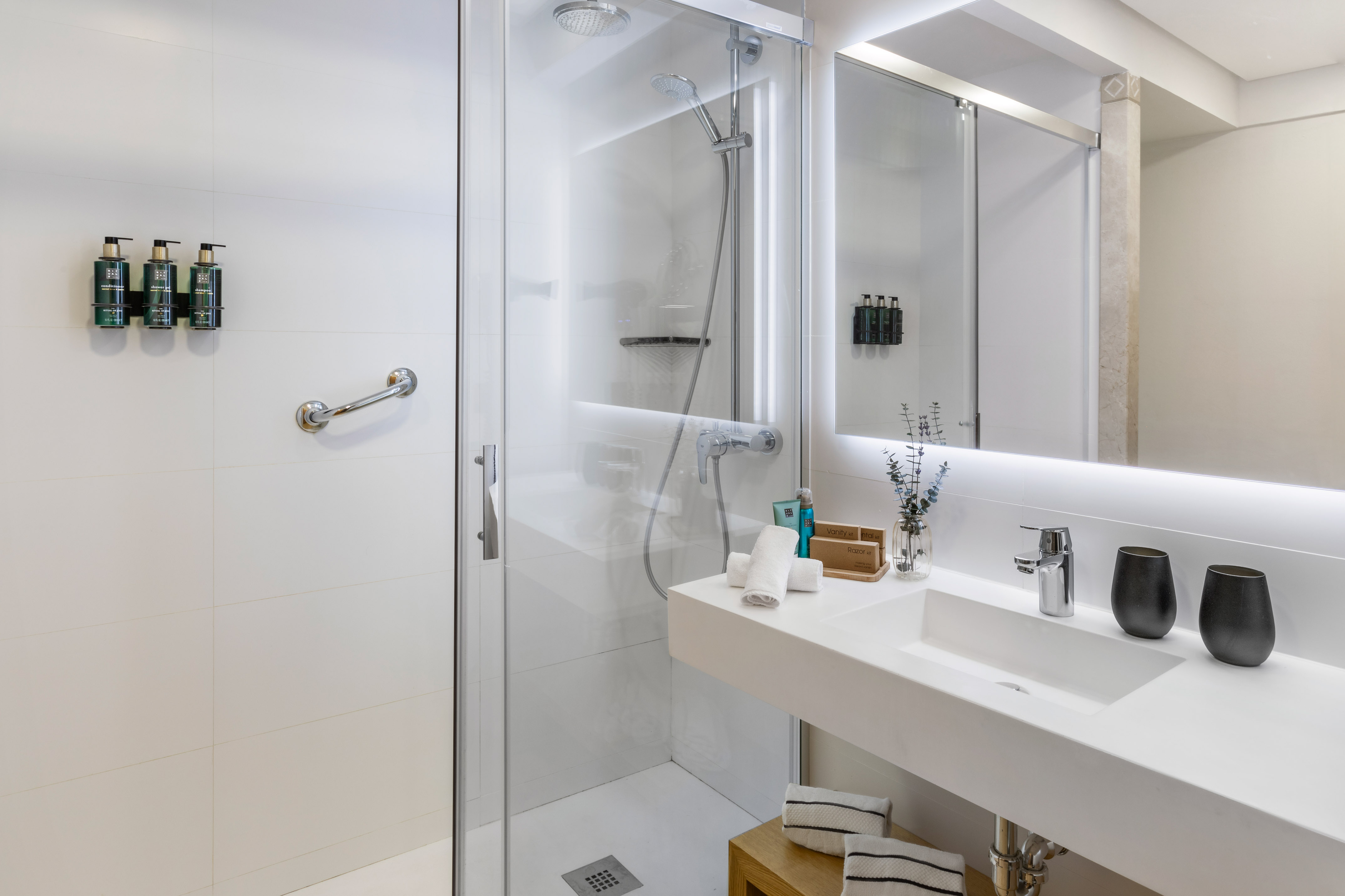Modern white bathroom: walk-in shower, vanity, backlit mirror, and grab bar.