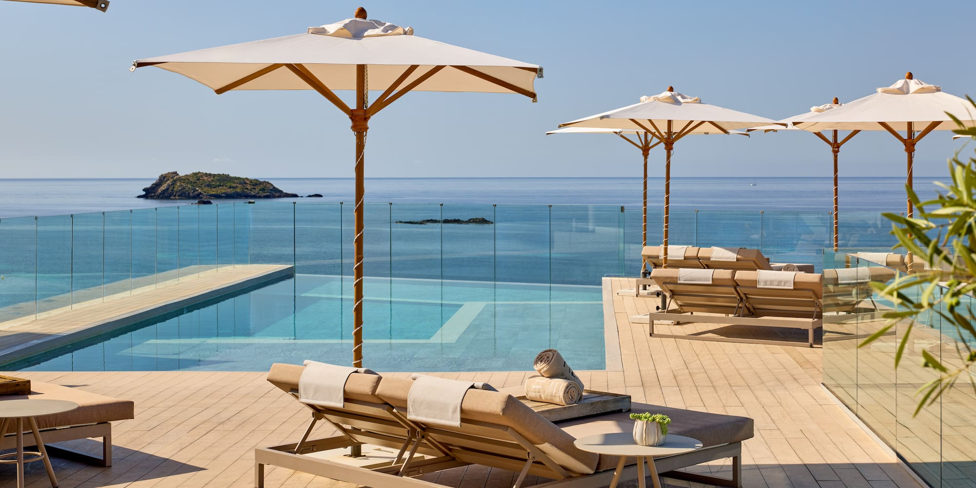 Luxury hotel infinity pool overlooking ocean, sun loungers, and umbrellas.